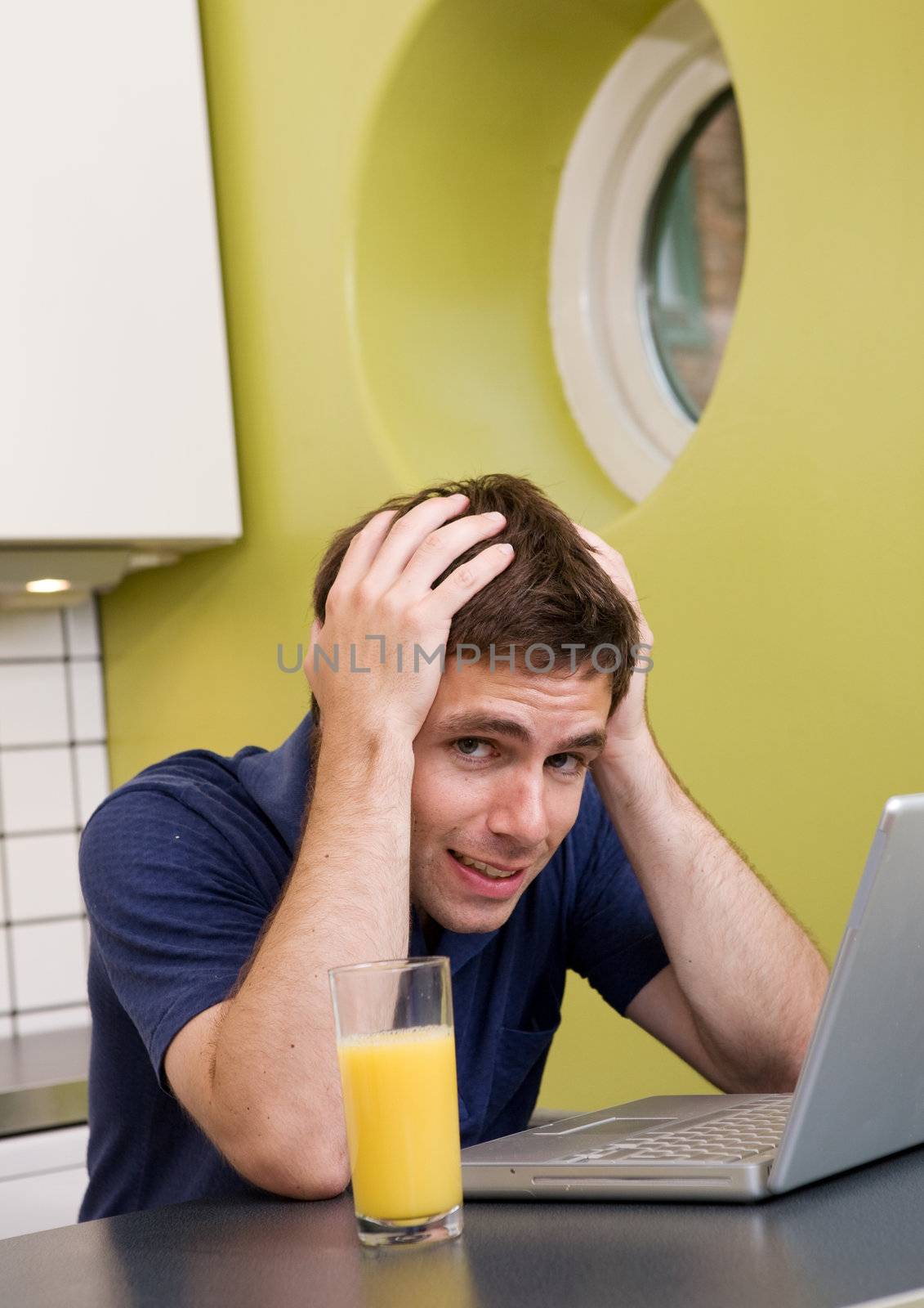 A worried computer user sits in his kitchen with a desperate look on his face