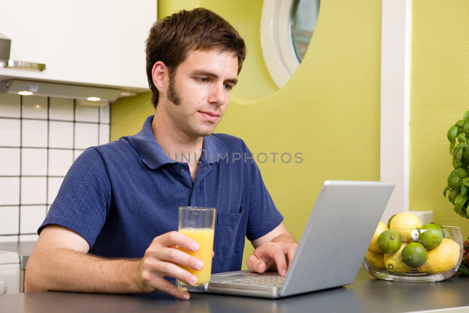 A young male works on the computer in the kicthen with a glass of orange juice