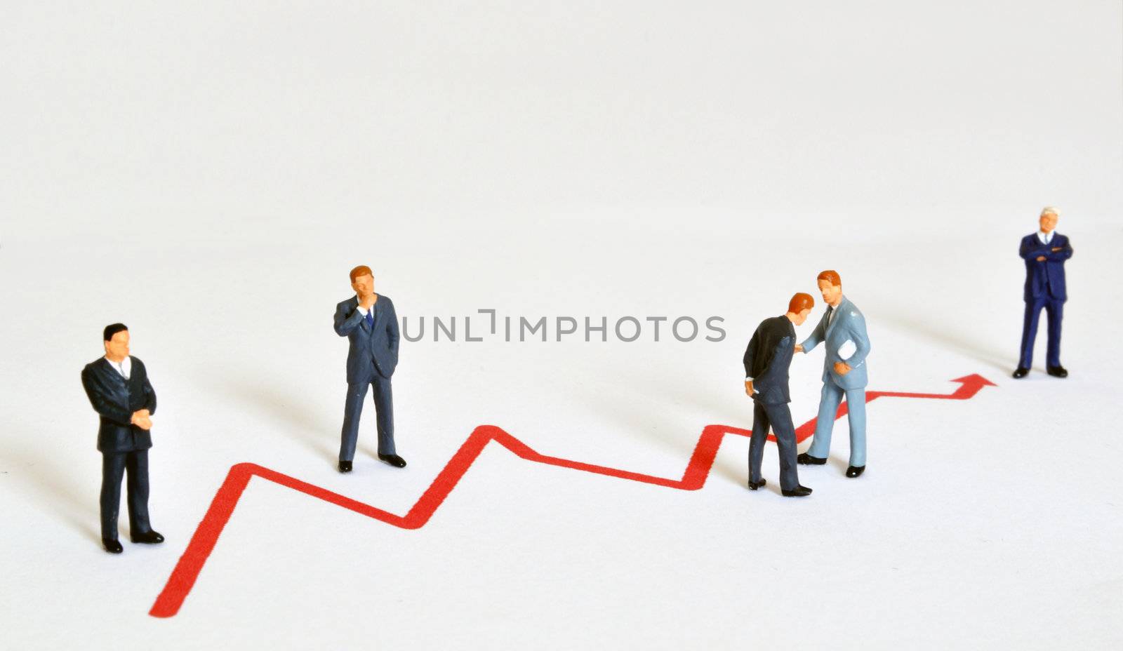 Group of managers (model railroad figures) positiones around graph showing rising business development.