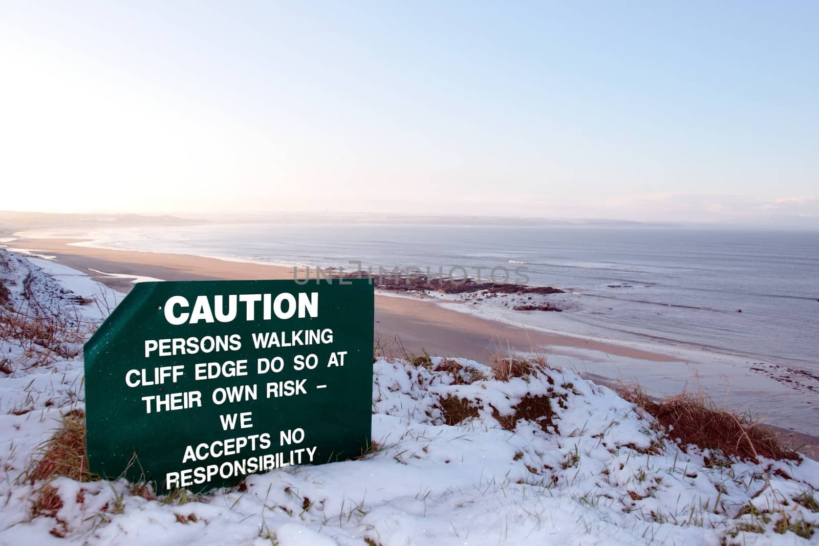 a caution sign on a cliff edge in snow covered ballybunion