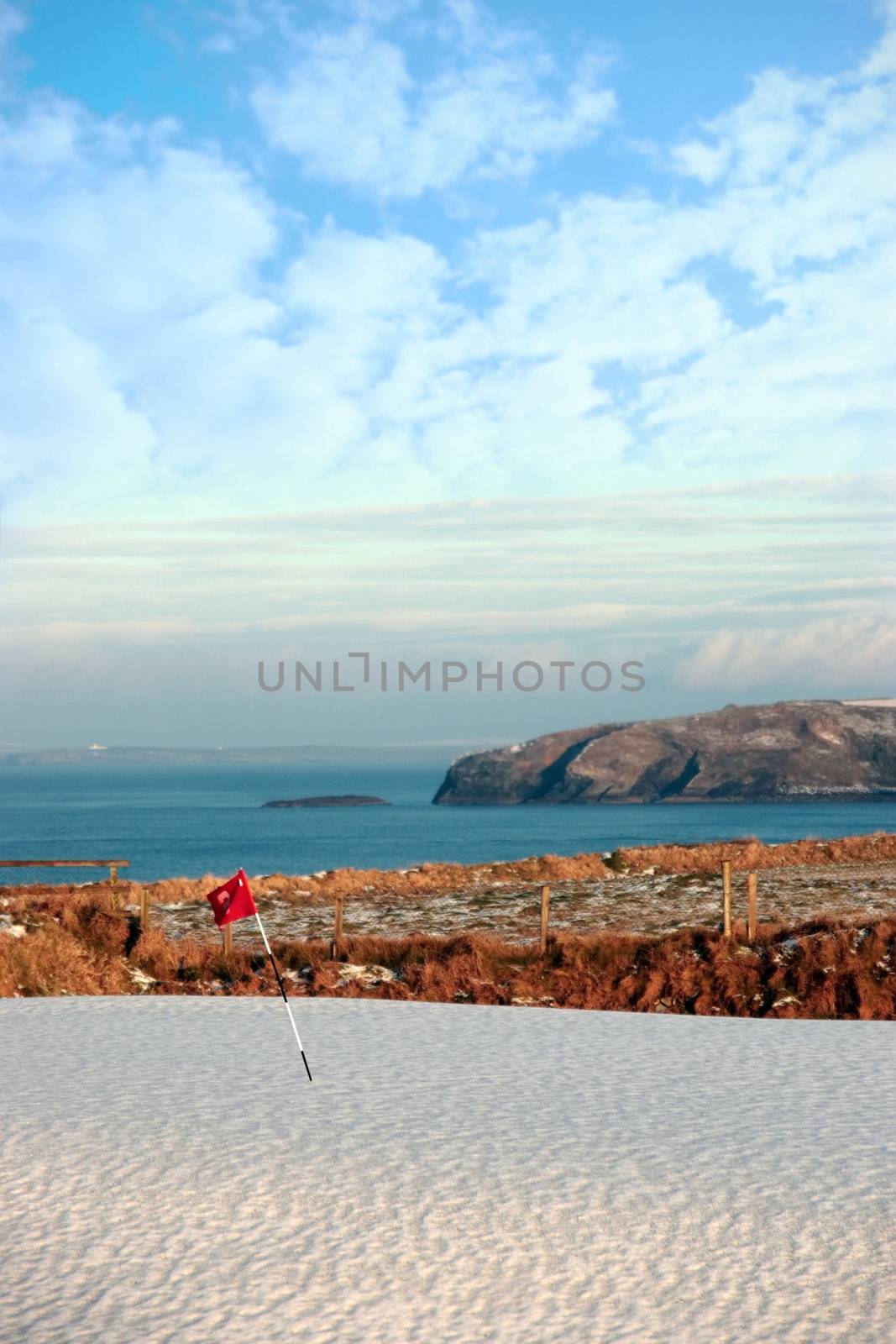 snow covering on a golf course in ireland in winter with sea and cliffs in background
