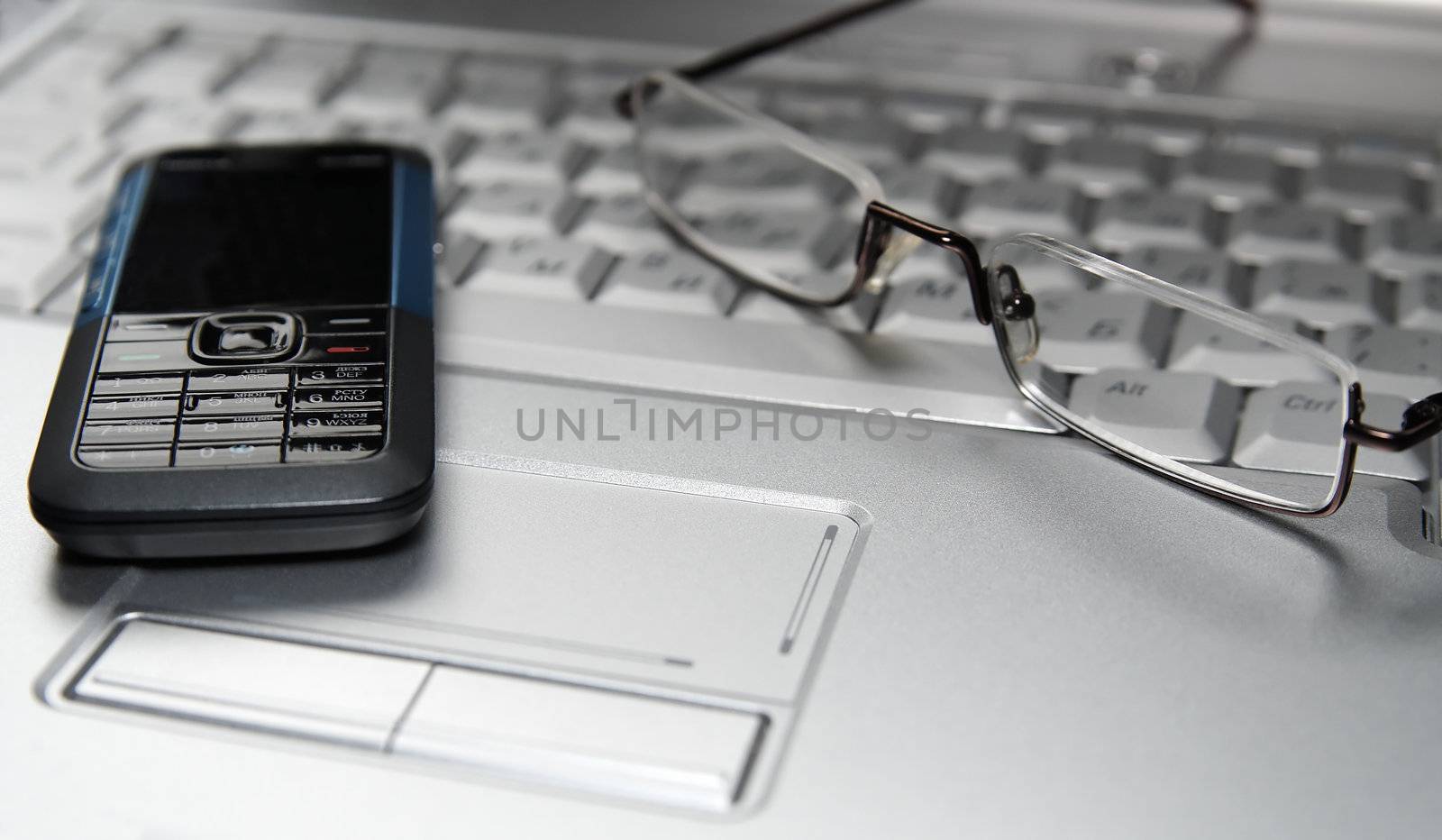 Mobile phone and glasses on laptop. Selective focus by serpl