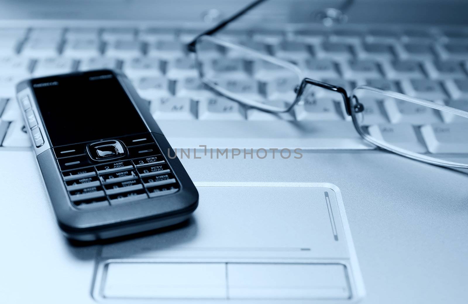 Blue tinted image of laptop with glasses and cellular phone