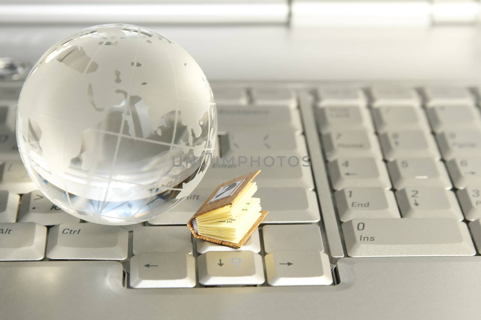 Little book and glass globe on laptop keyboard by serpl