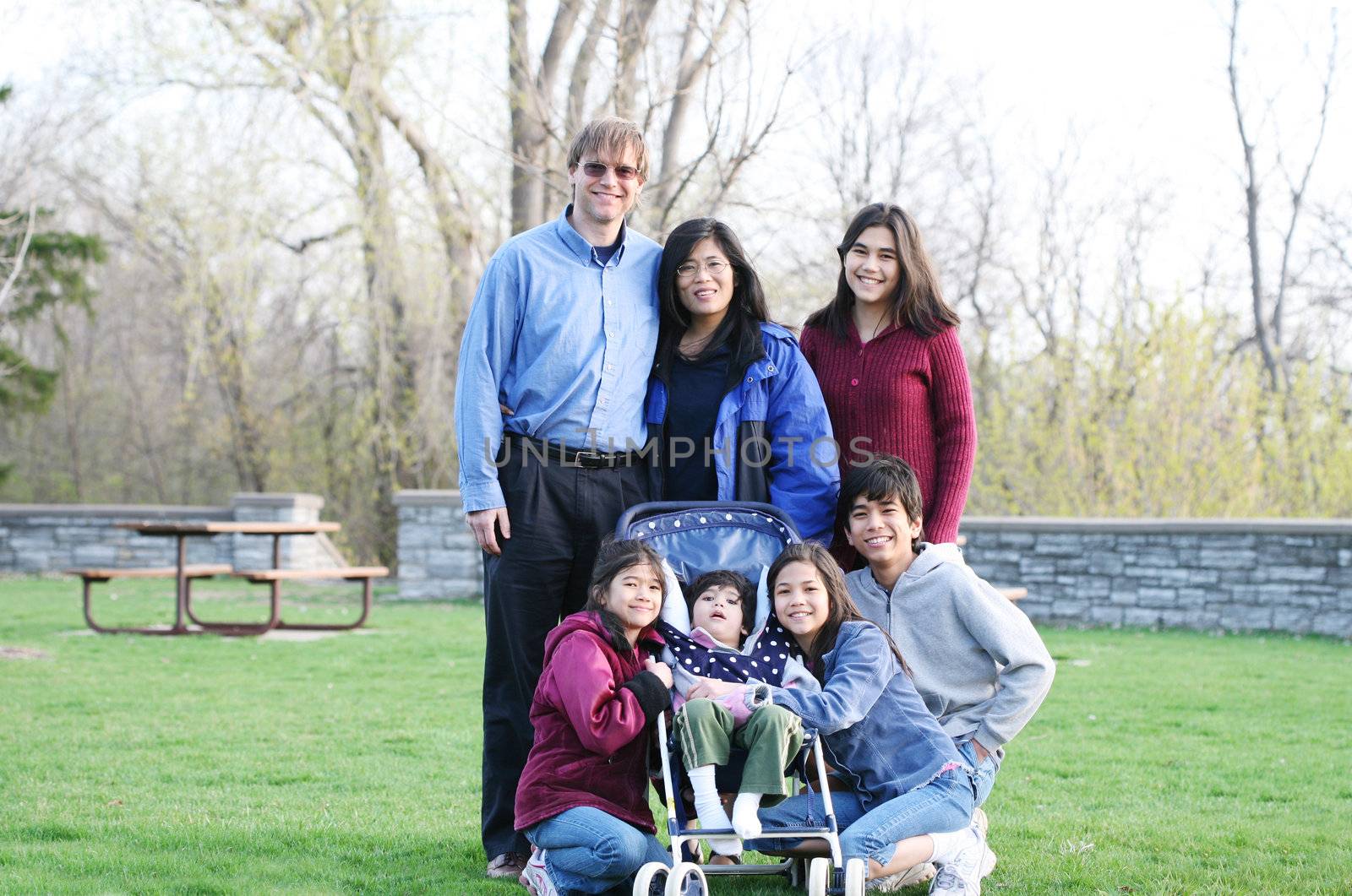 Beautiful Interracial family of seven outdoors in summer. Child in stroller is disabled with cerebral palsy