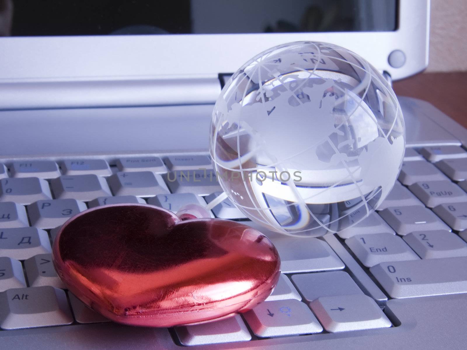 Heart and glass globe on keyboard of notebook. Background