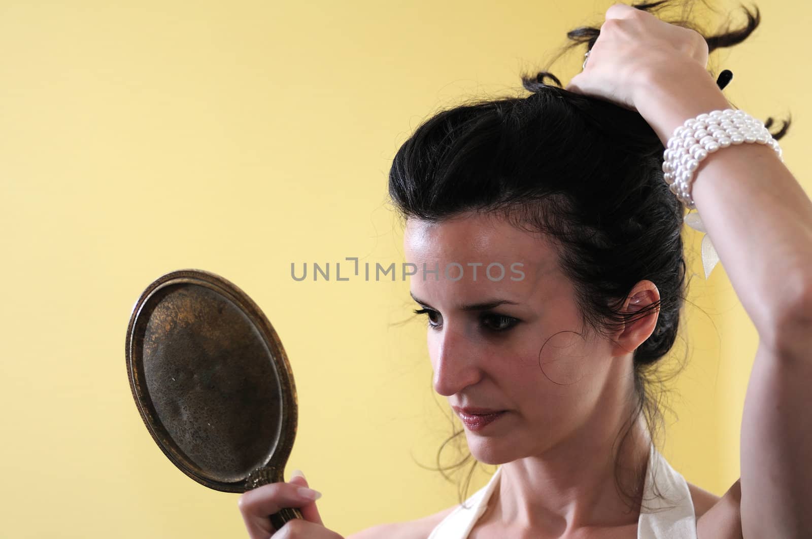 A young woman fixes her hair while gazing into an antique hand mirror.
