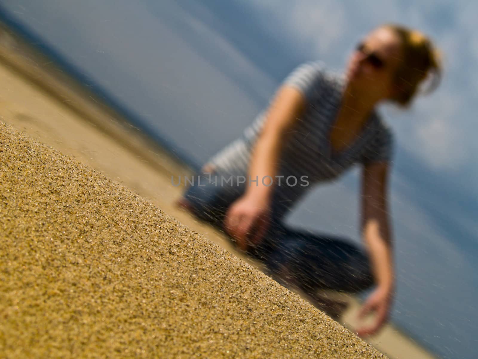 Young blond-hairy girl sitting an a sea beach. Focus on sand