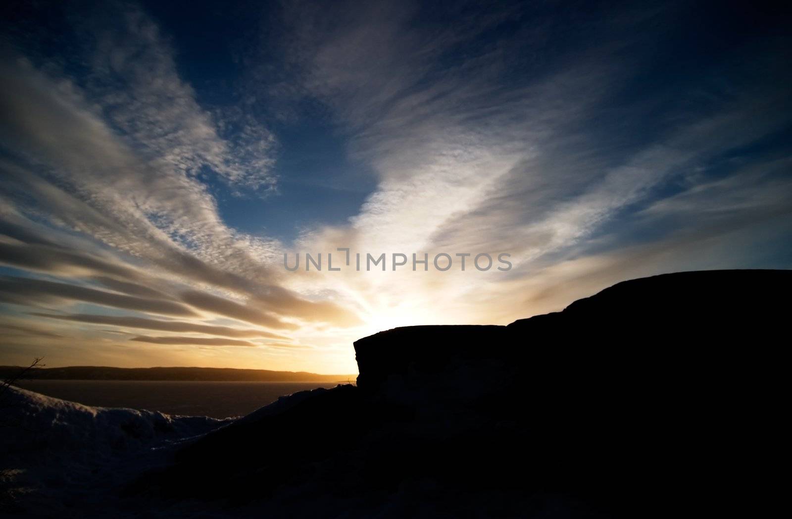 A rock landscape near the ocean during a sunset and a dramatic sky.