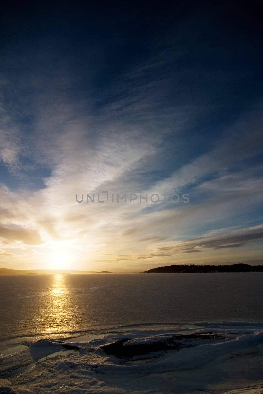 A golden sunset going down behind a hill over a frozen lake - fjord.  Oslo fjord in March.