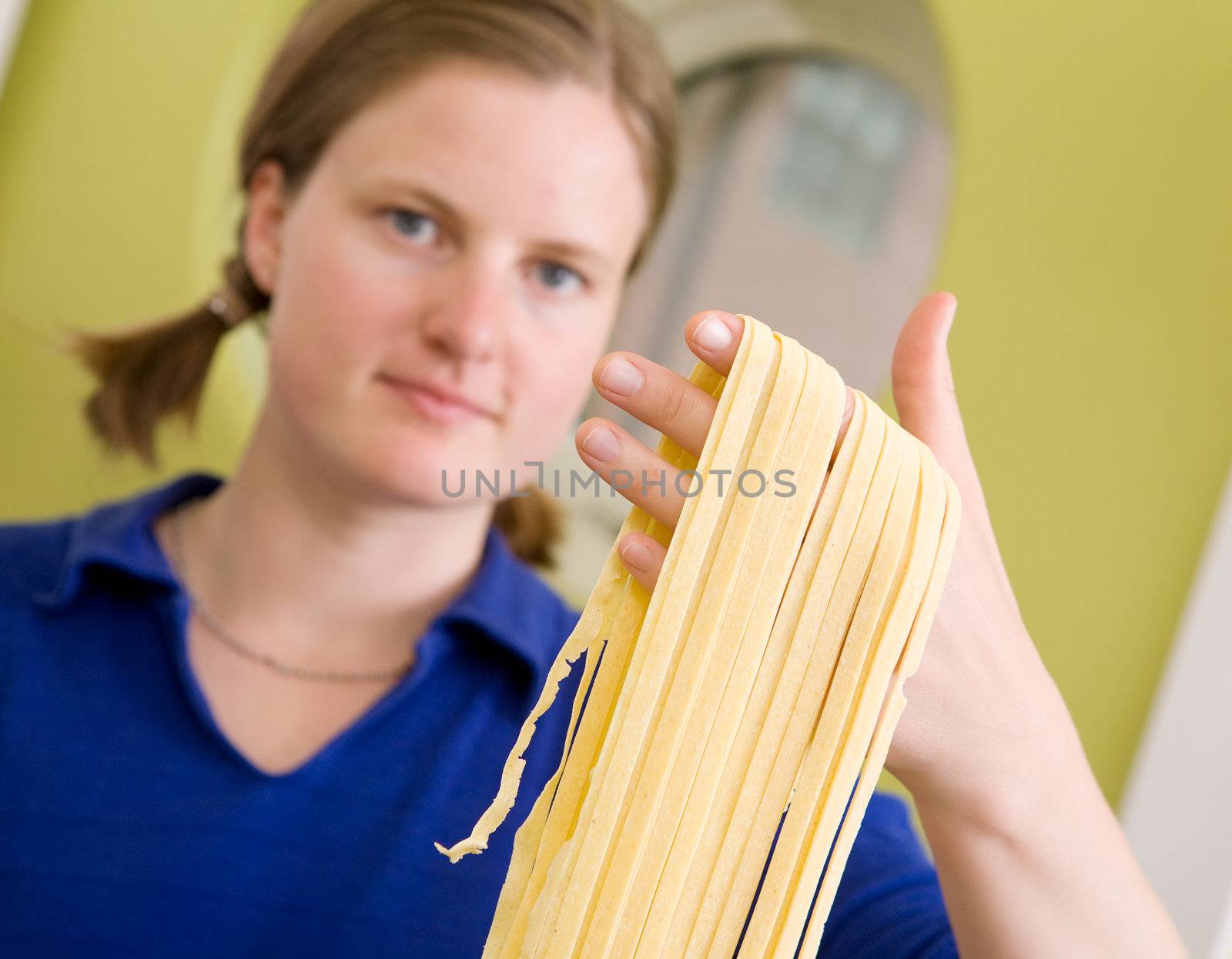 A proud young woman with fresh homemade fettuccine looks at the camera- shallow depth of field with focus on the pasta