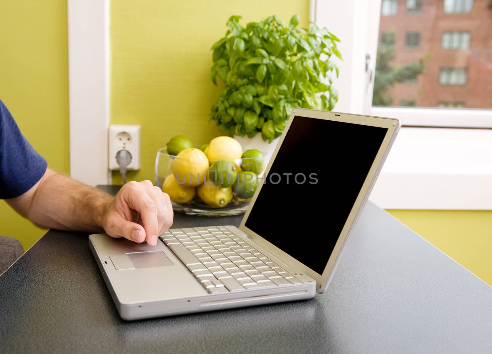 A computer in the kitchen with a male hand using the touch pad.  The laptop has a completely black screen for easy editing.