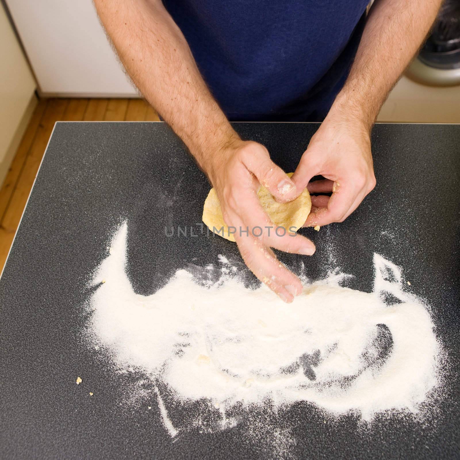 A detail image of a male making fresh pasta on the counter.  The pasta dough is being flatened before rolling through the pasta machine