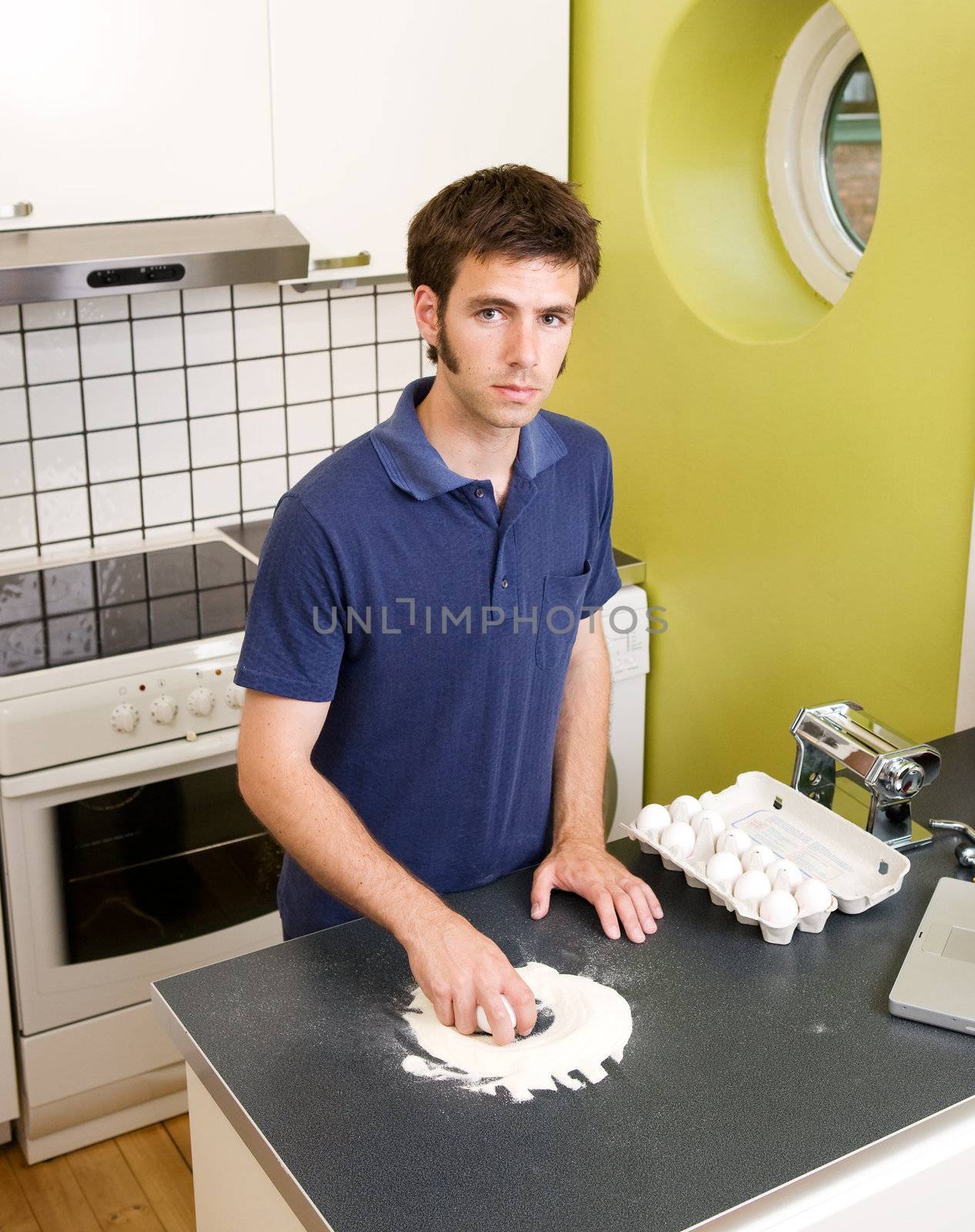 A young man making pasta at home in an apartment kitchen.