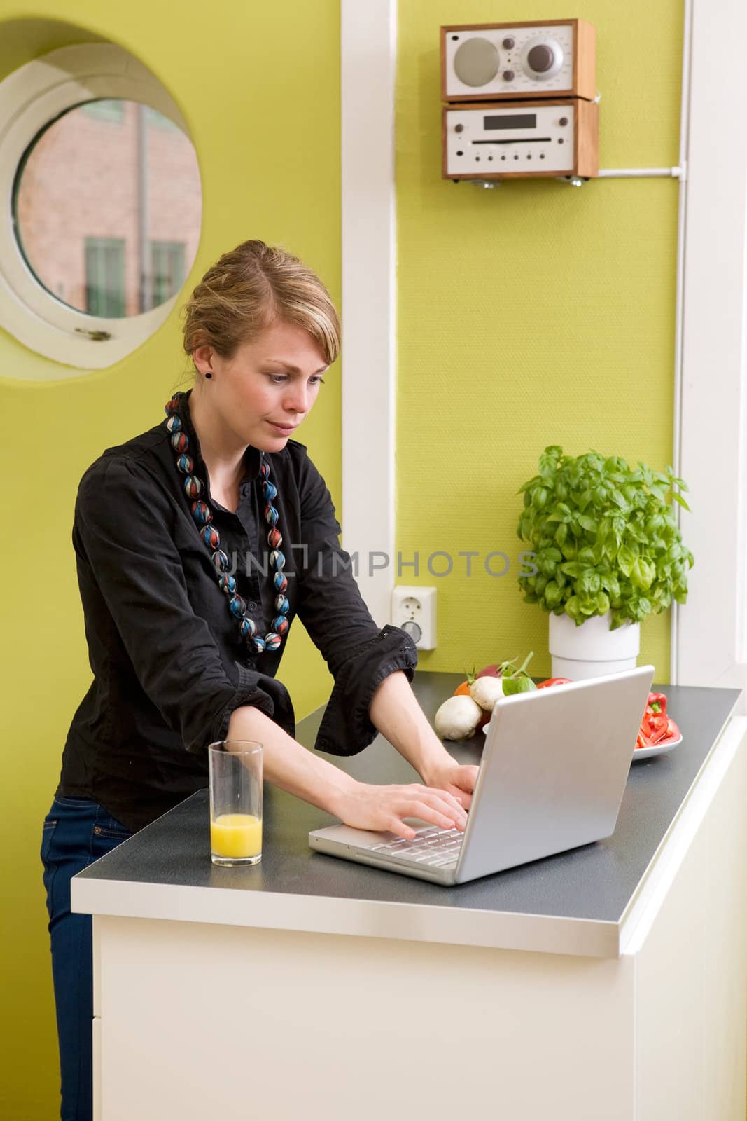 A female uses the computer on the kitchen counter while having a light snack of vegetables