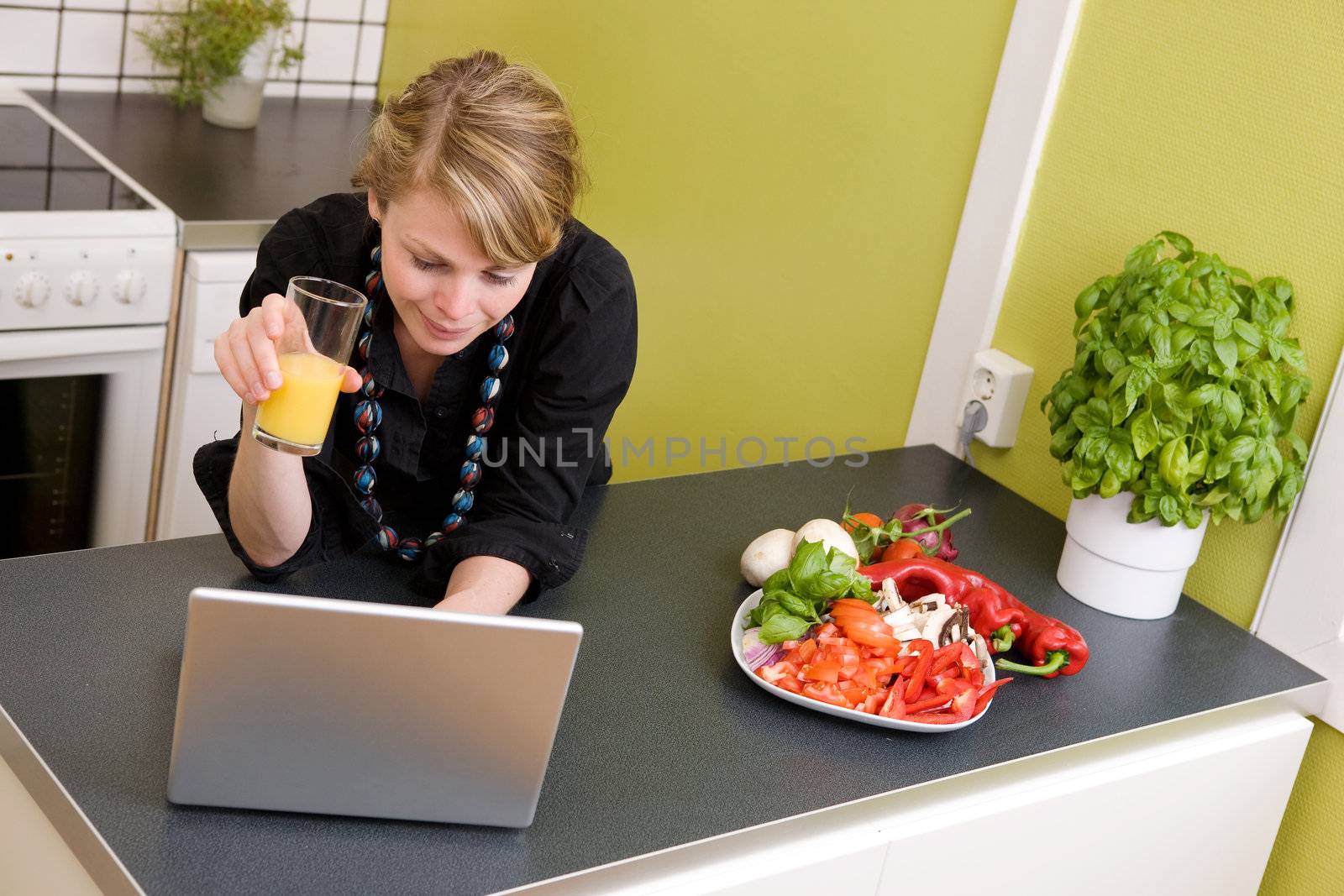 A young female surfs the internet while enjoying a light healthy snack of vegetables and juice.