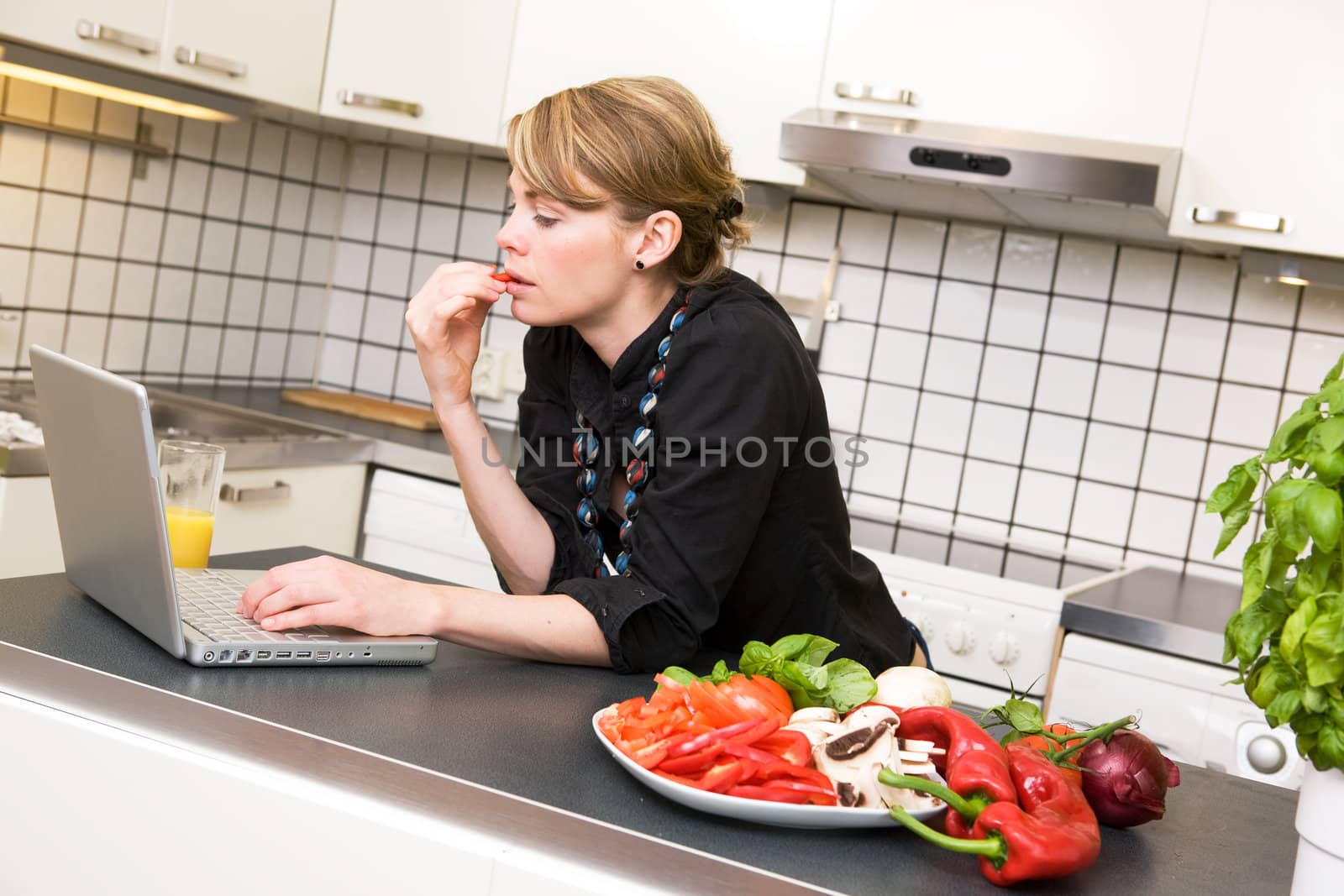 A young female woman using the computer in the kitchen over a small healthy lunch of vegetables;