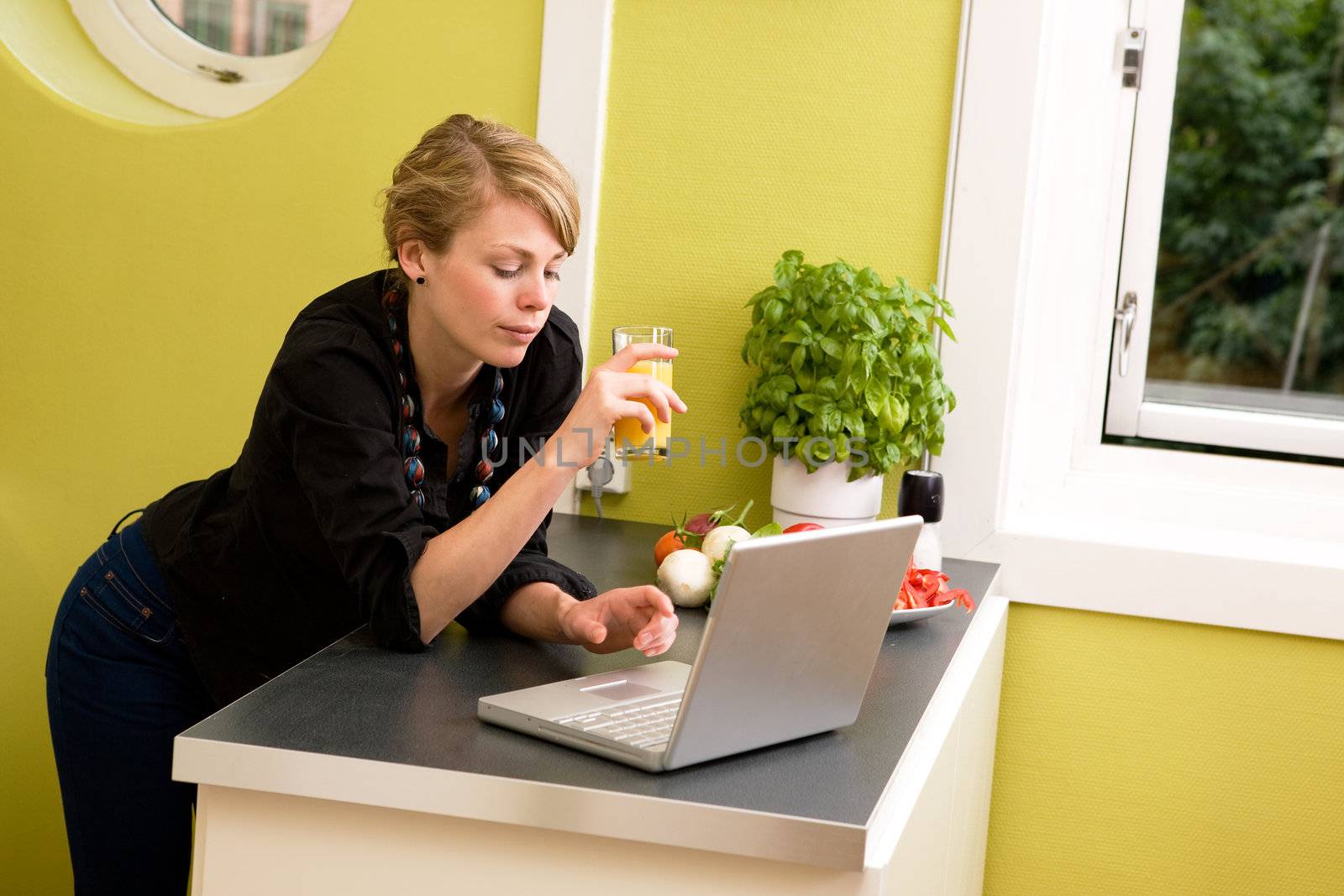 A woman using her laptop over a light healthy snack in the kitchen.