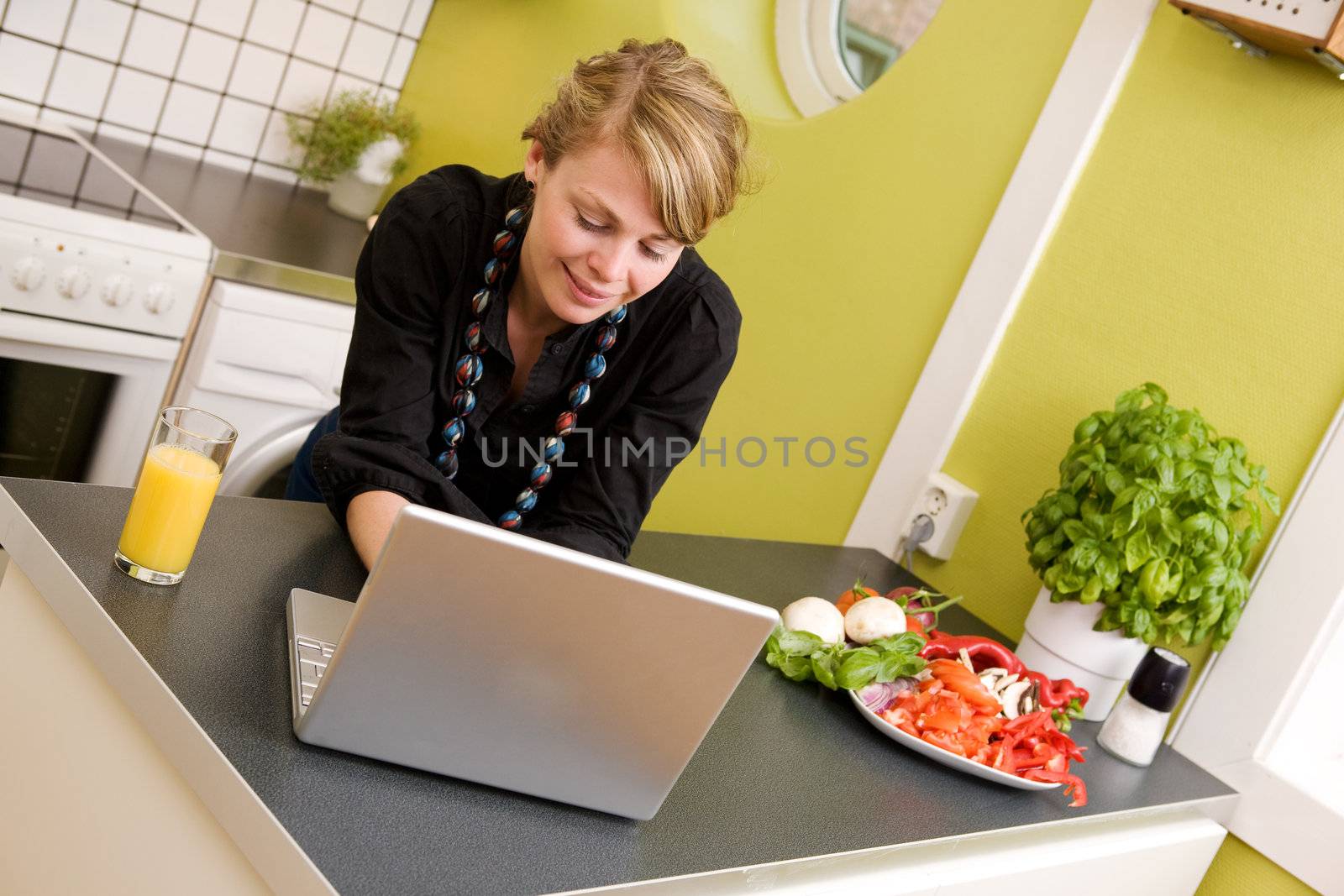 A young woman using the computer while eating a healthy snack in an apartment kitchen;