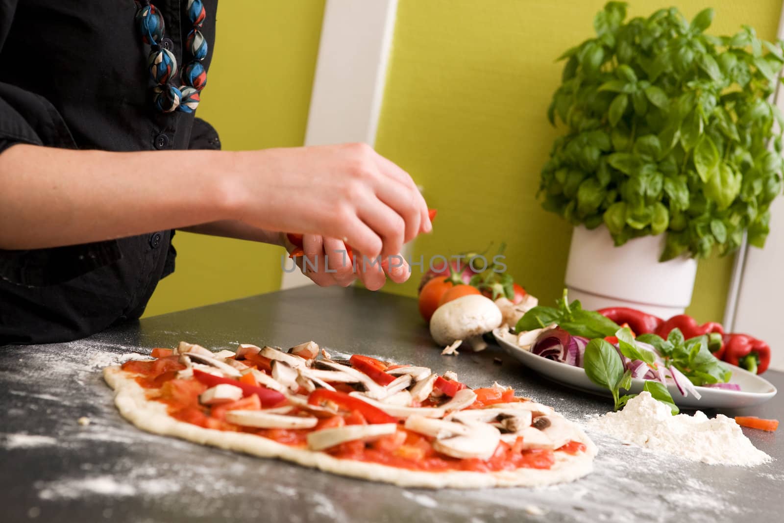 A young female making an italian style pizza at home in her apartment kitchen. - Shallow depth of field is used, with focus on the pizza and hands.