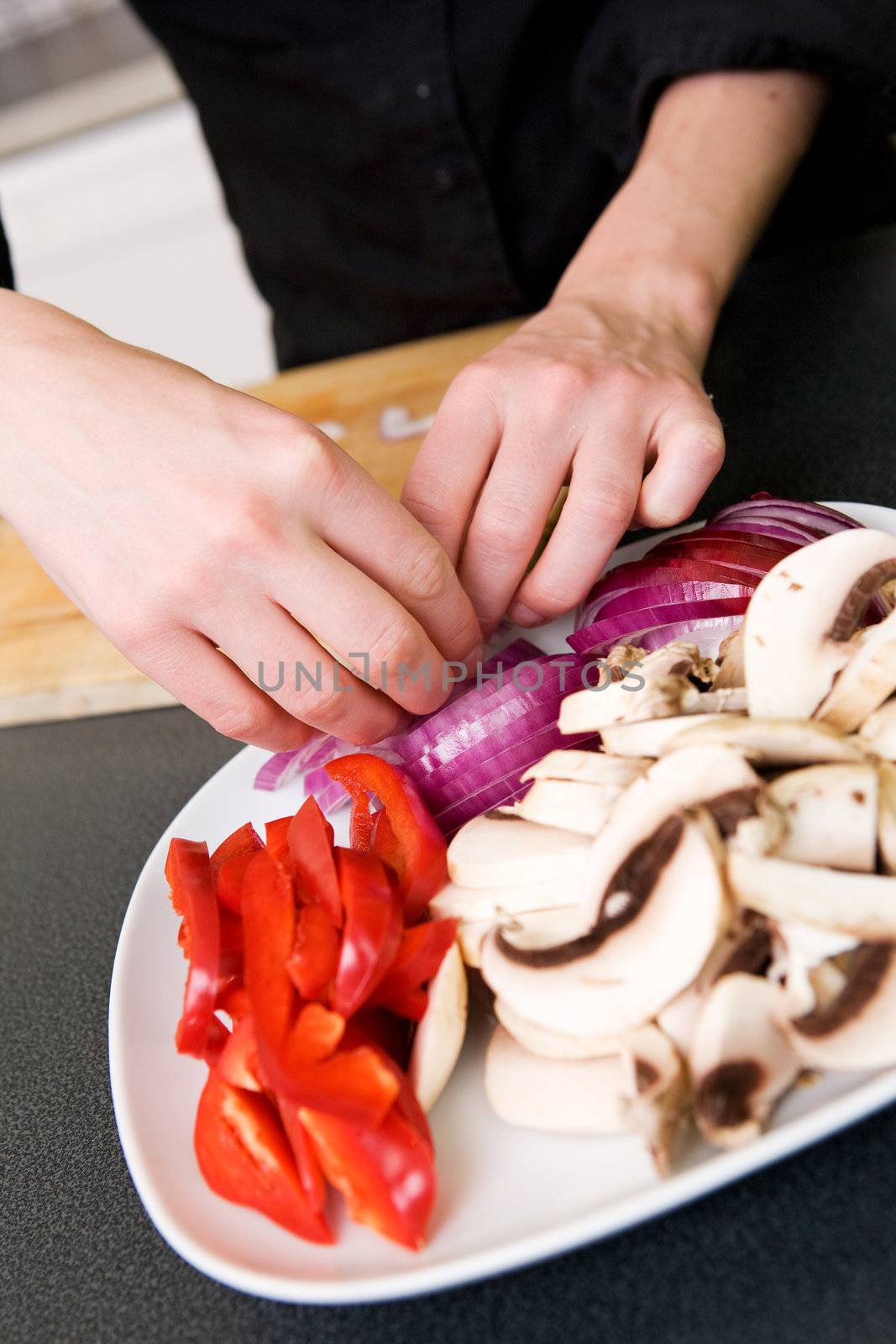 A female puts the finishing touches on a simple vegetable platter consiting of red peppers, onions and mushrooms.  