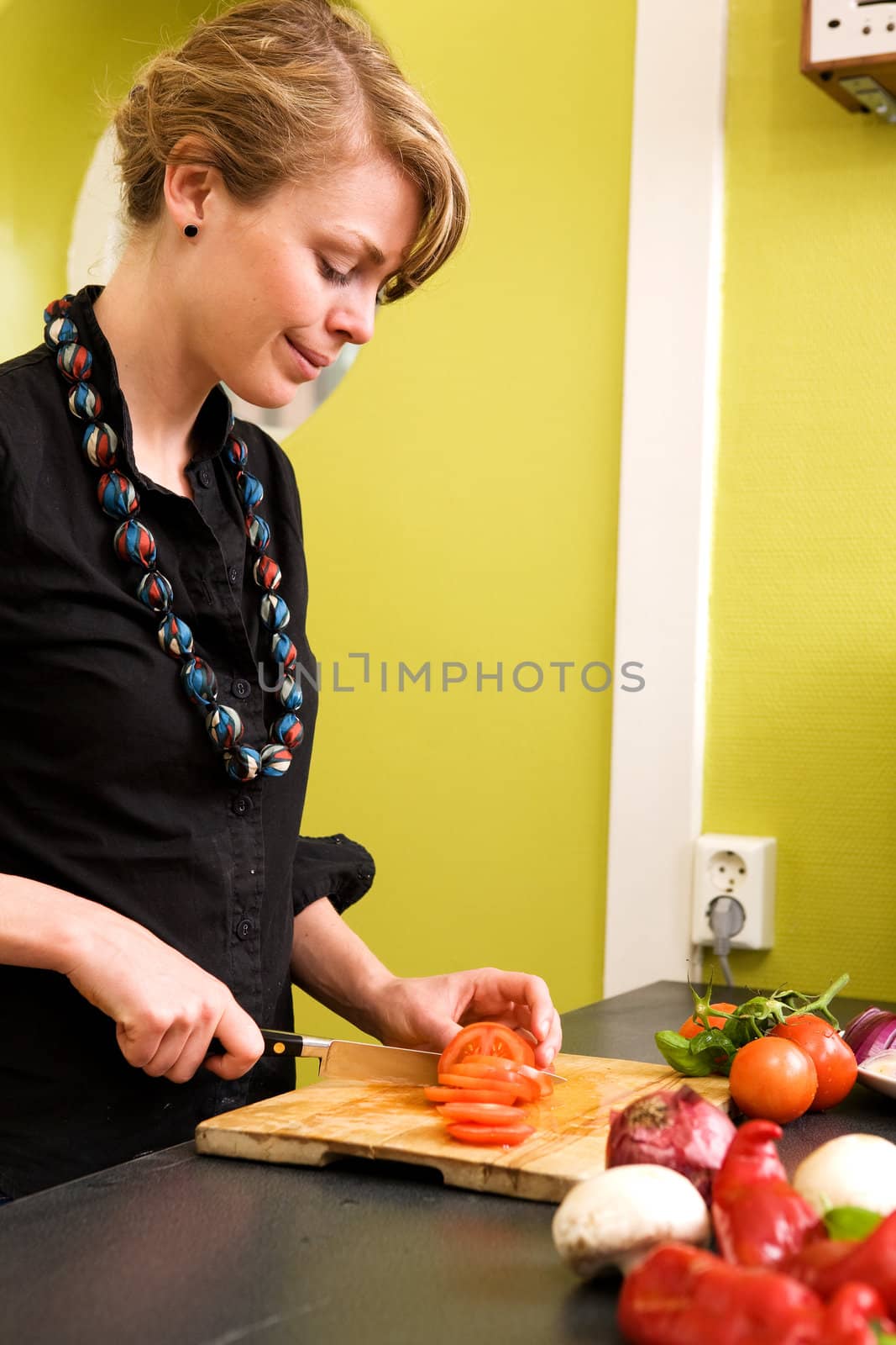 A female is at home in the kitchen slicing tomatoes for a pizza.