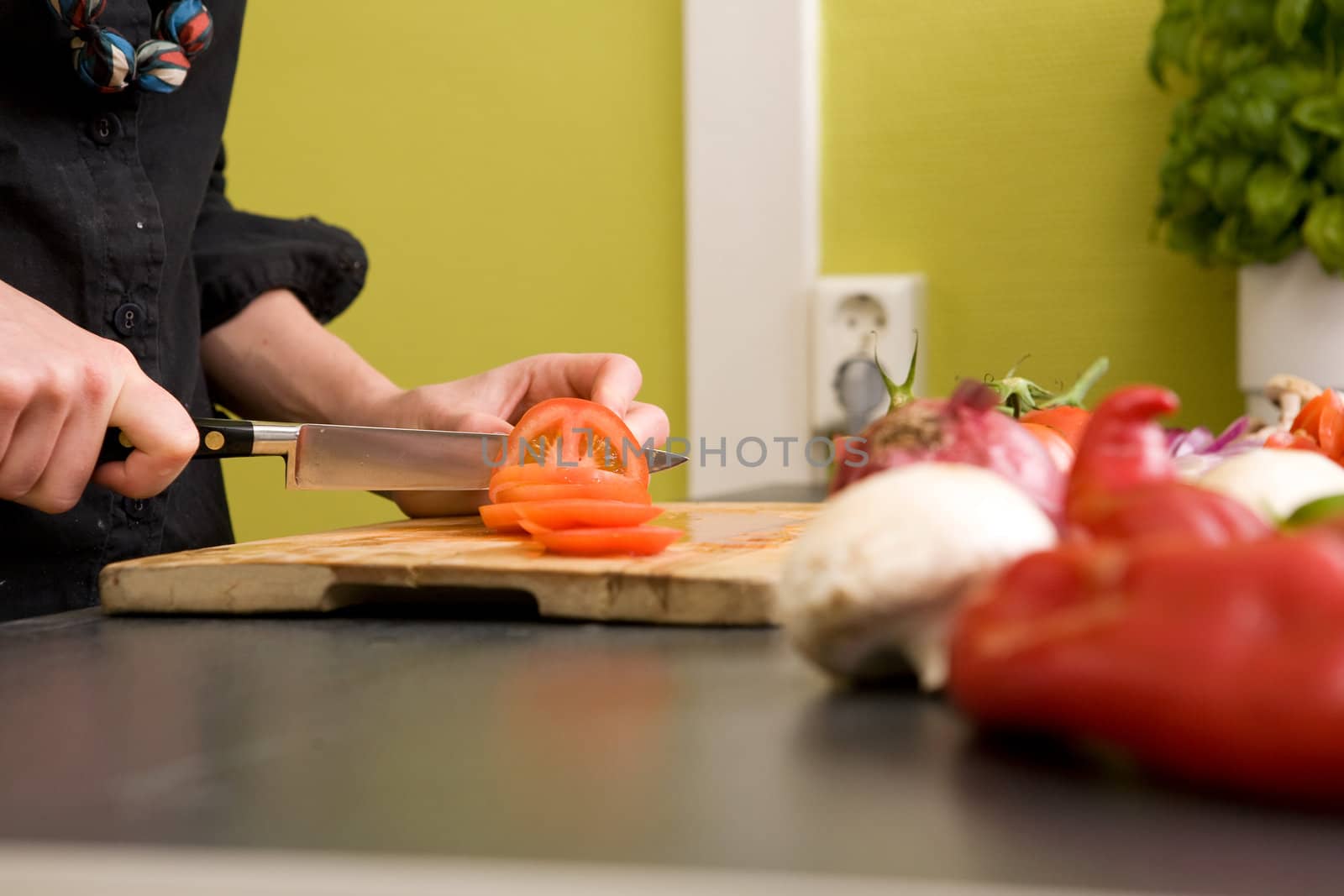 A detail image of a woman slicing tomatoes on a cutting board at home. - shallow depth of field with the focus on the tomato and knife