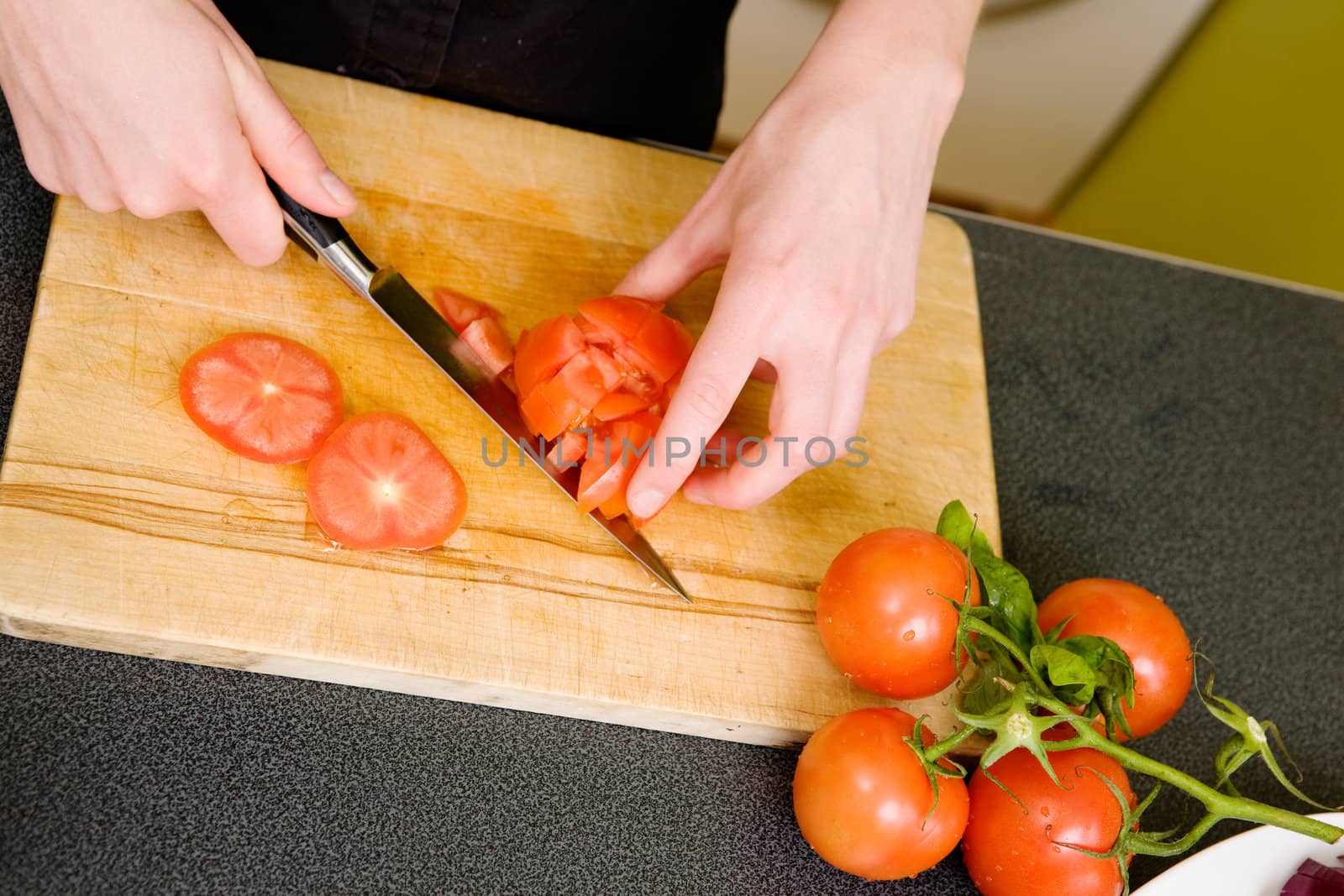 Dicing tomatoes on a cutting board viewed from above.