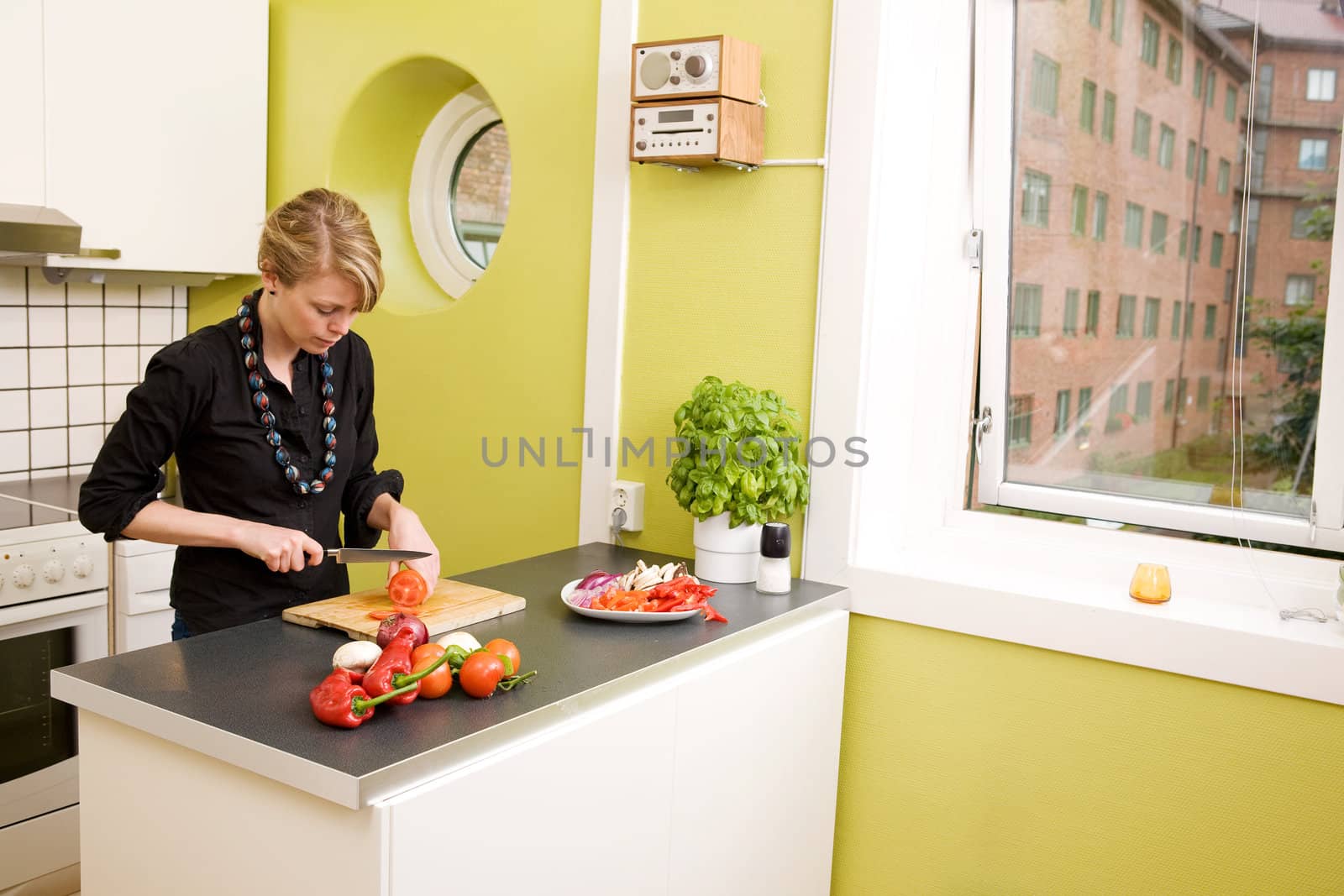 A female in her apartment kitchen preparing supper and cutting tomatoes;