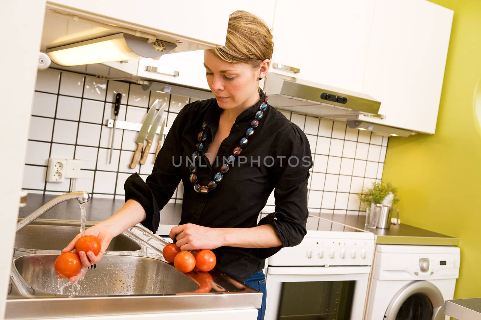 A woman is washing tomatoes in the sink at home in the kitchen. 