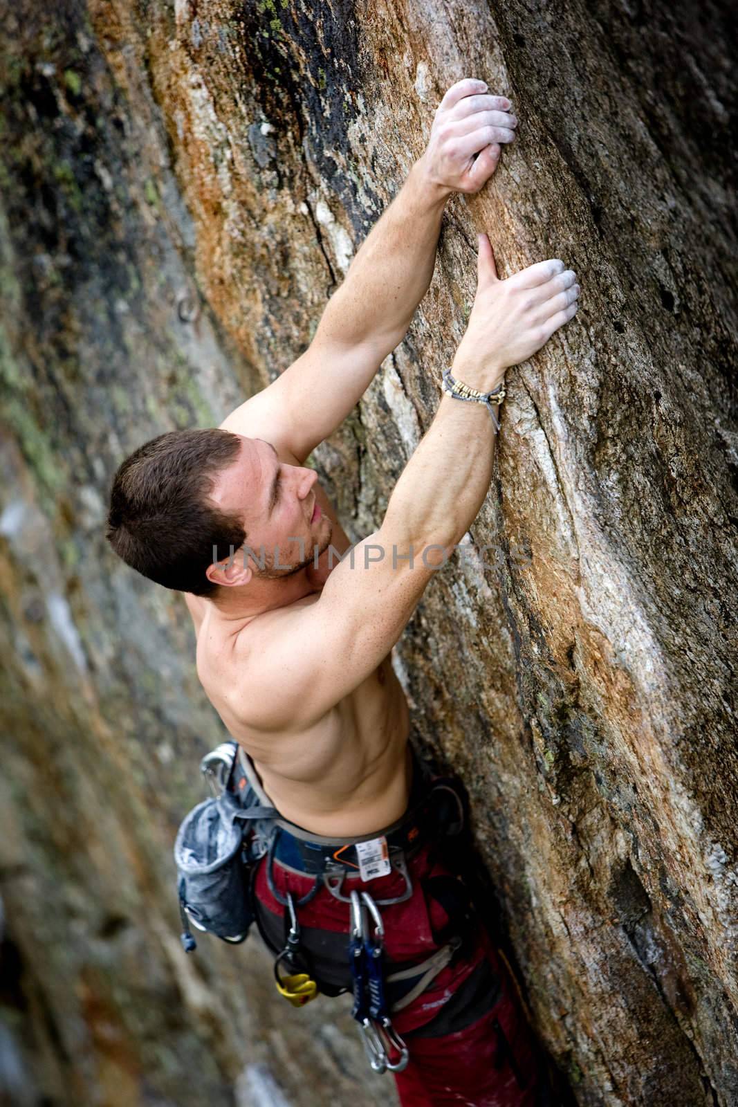 A male climber, viewed from above, climbs a very high and steep crag. 