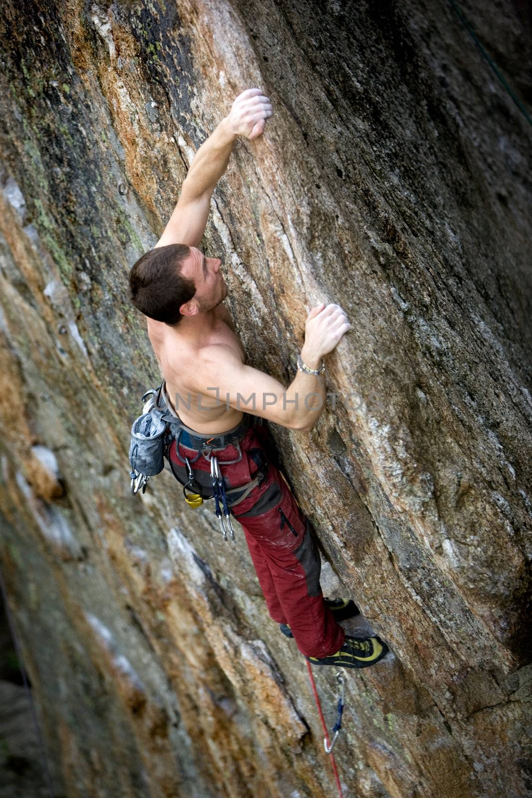 A male climber, viewed from above, climbs a very high and steep crag.