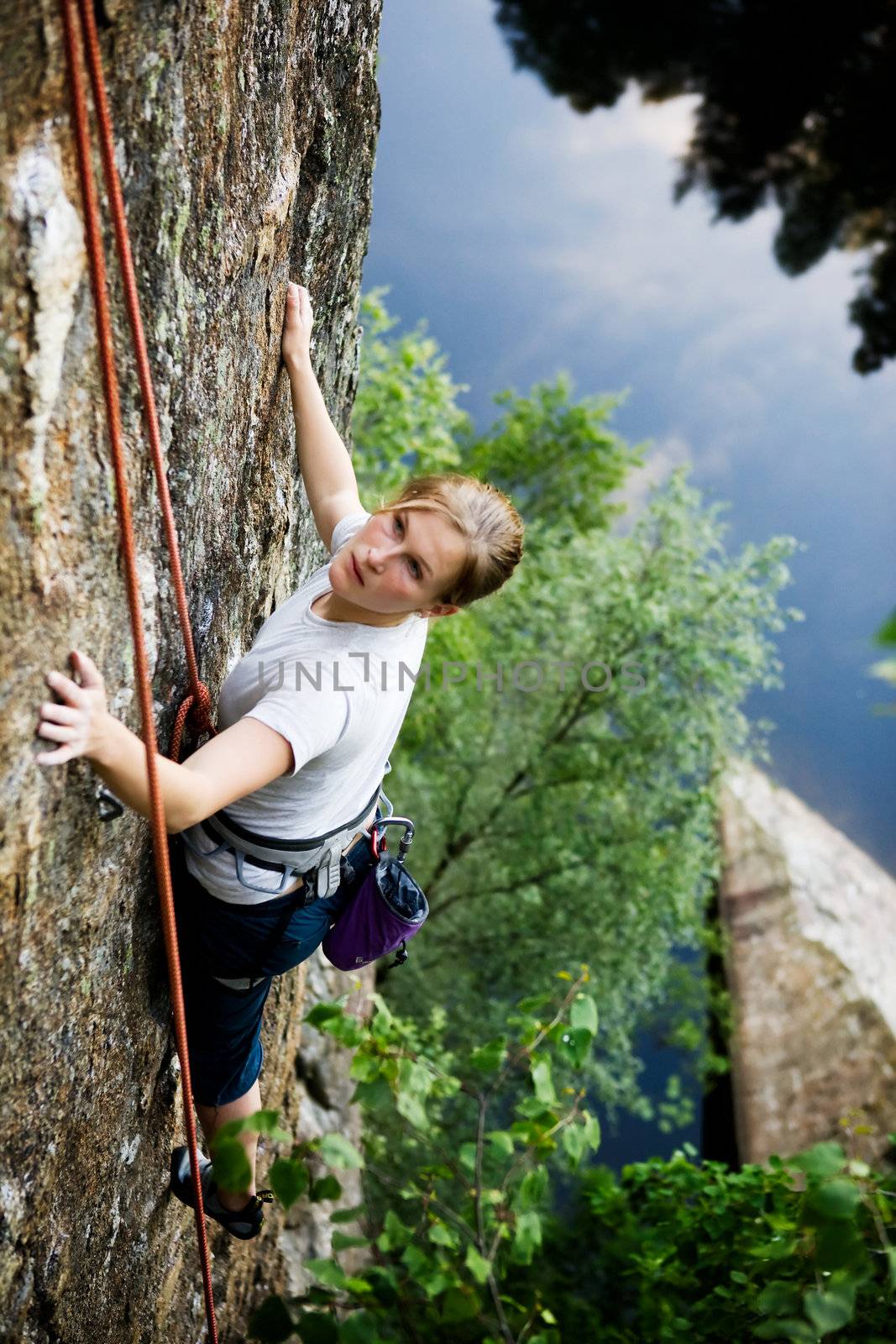 A female climber on a steep rock face looking for the next hold.  Shallow depth of field is used to isolate the climber.