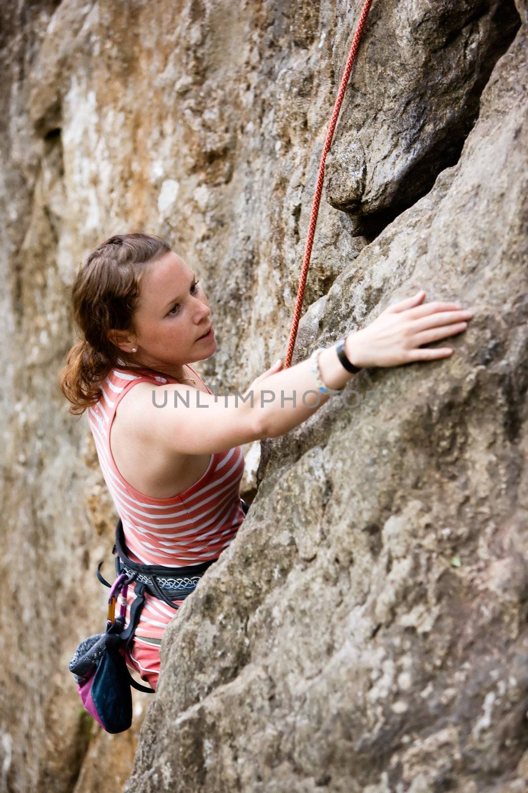 A female climber, climbing using a top rope on a steep rock face (crag).  A shallow depth of field has been used to isolated the climber, with the focus on the head and eyes.