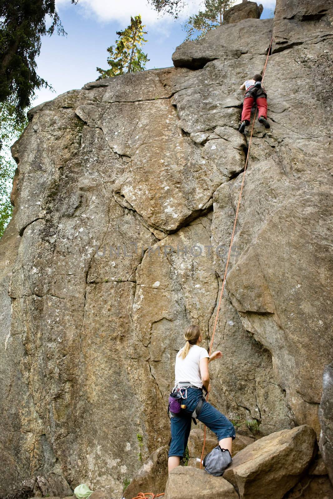 A female belaying a male on a steep rock face.