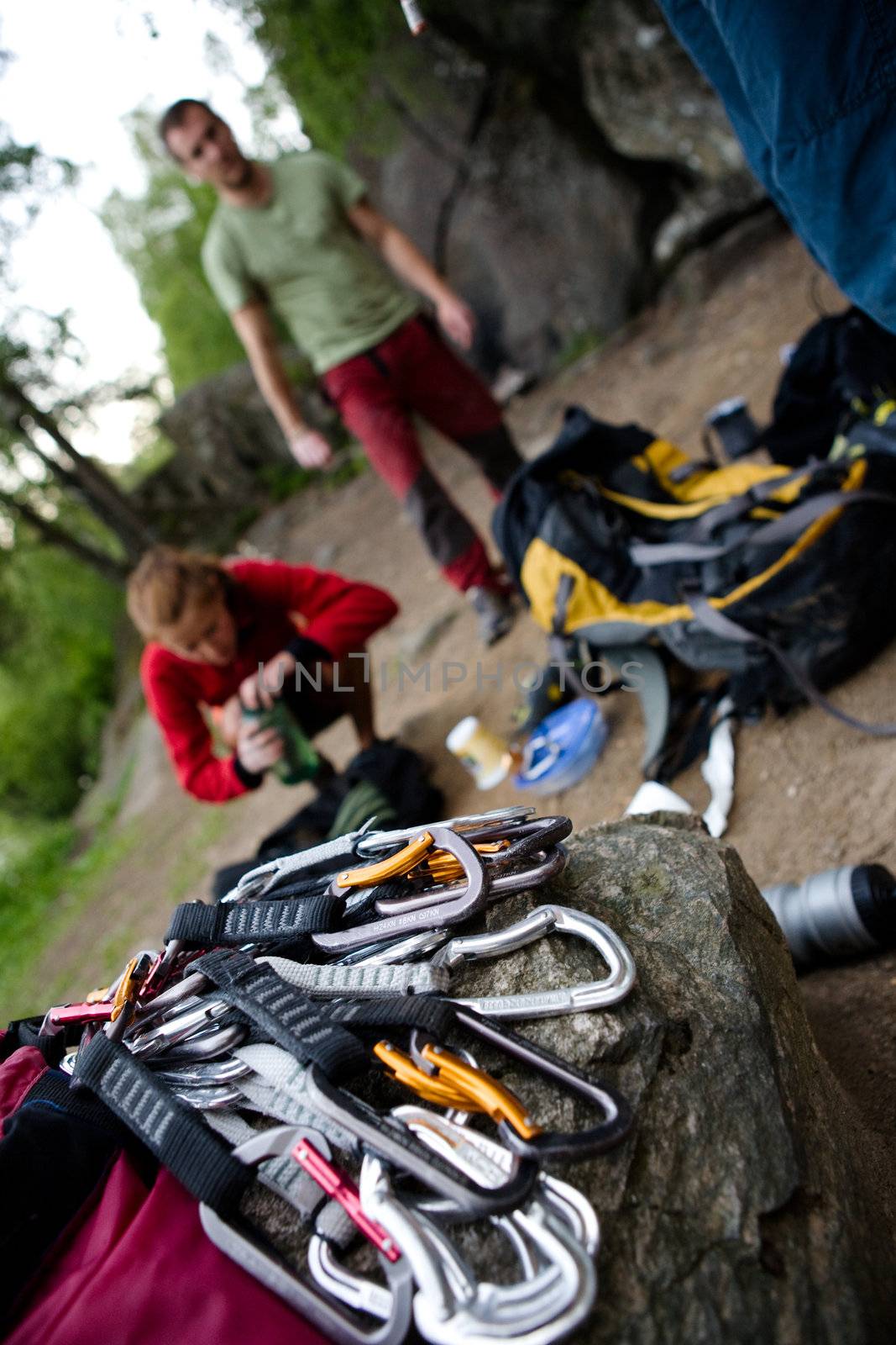 A pile of quick draw carabiners with climbers out of focus in the background.