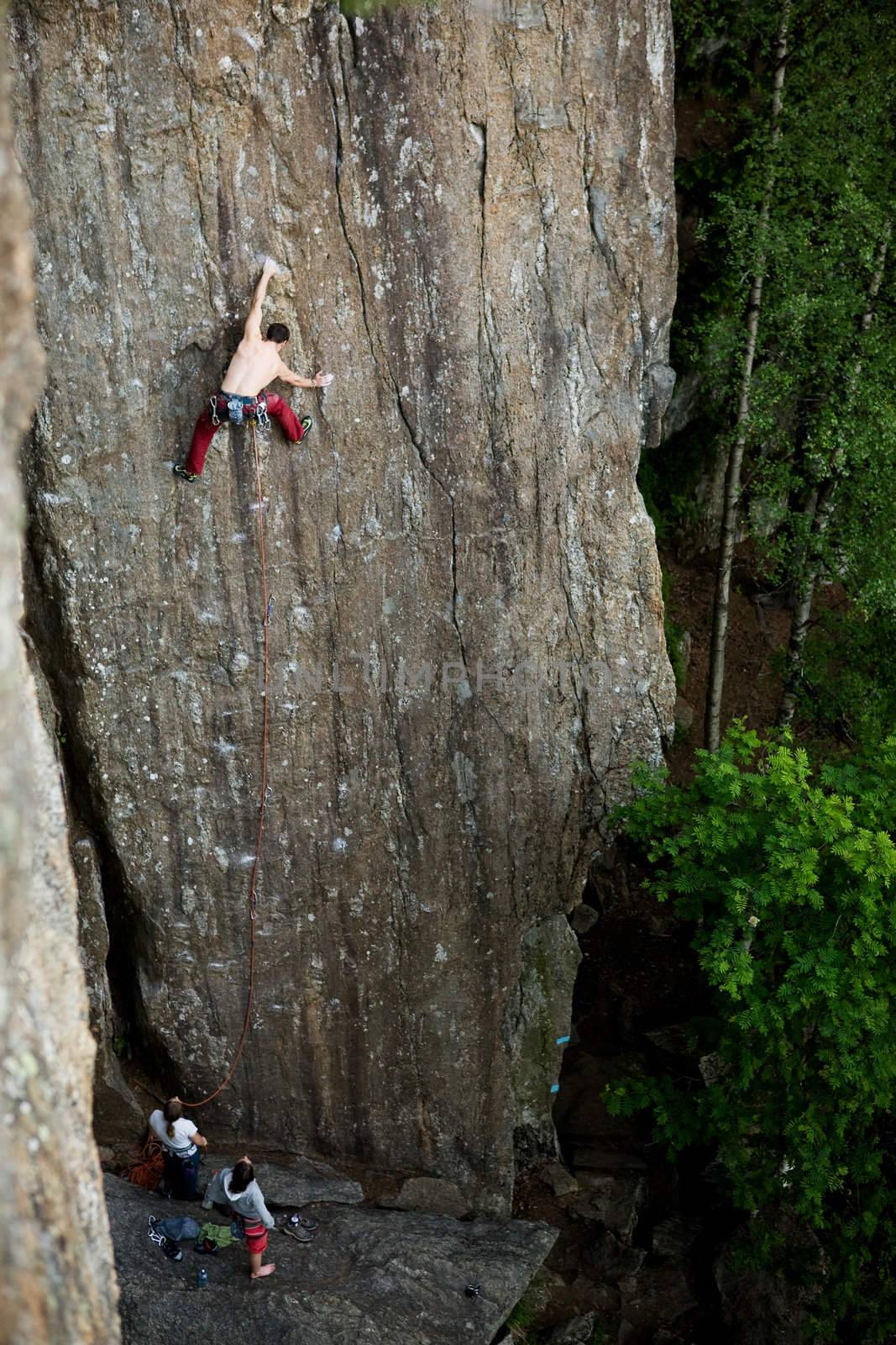 A male climber against a large rock face climbing lead.