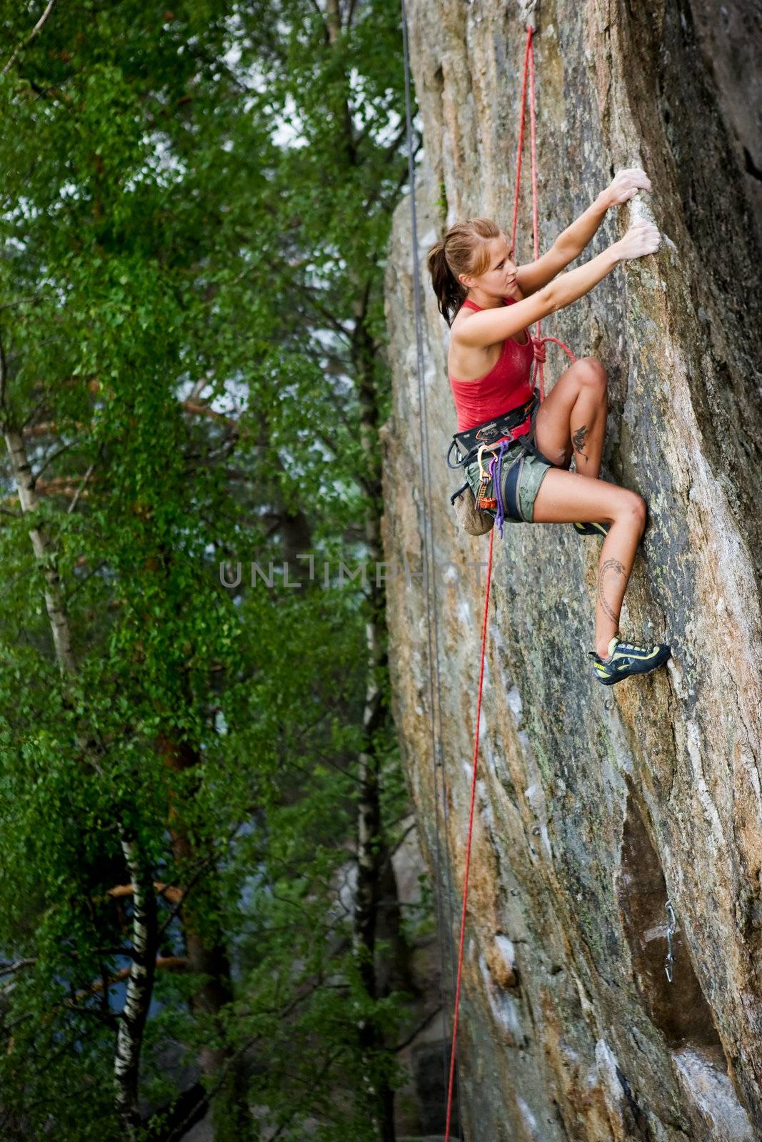 An eager female climber on a steep rock face looks for the next hold. Shallow depth of field is used to isolated the climber with the focus on the head.