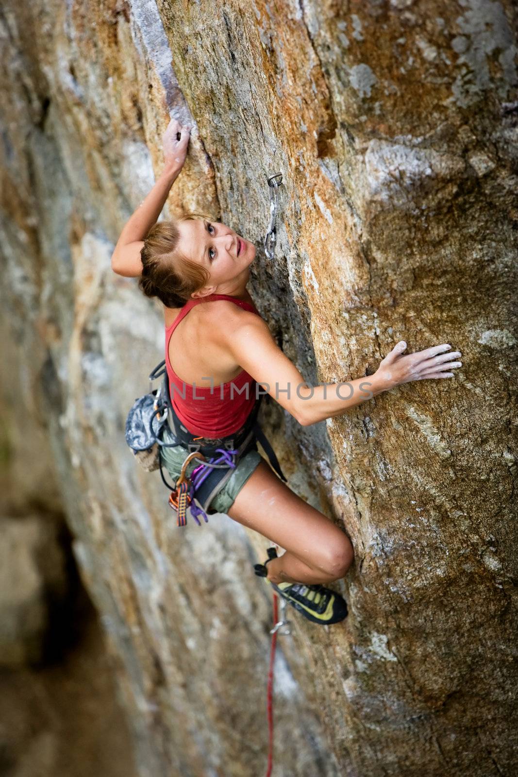 An eager female climber on a steep rock face looks for the next hold - viewed from above.  Shallow depth of field is used to isolated the climber.