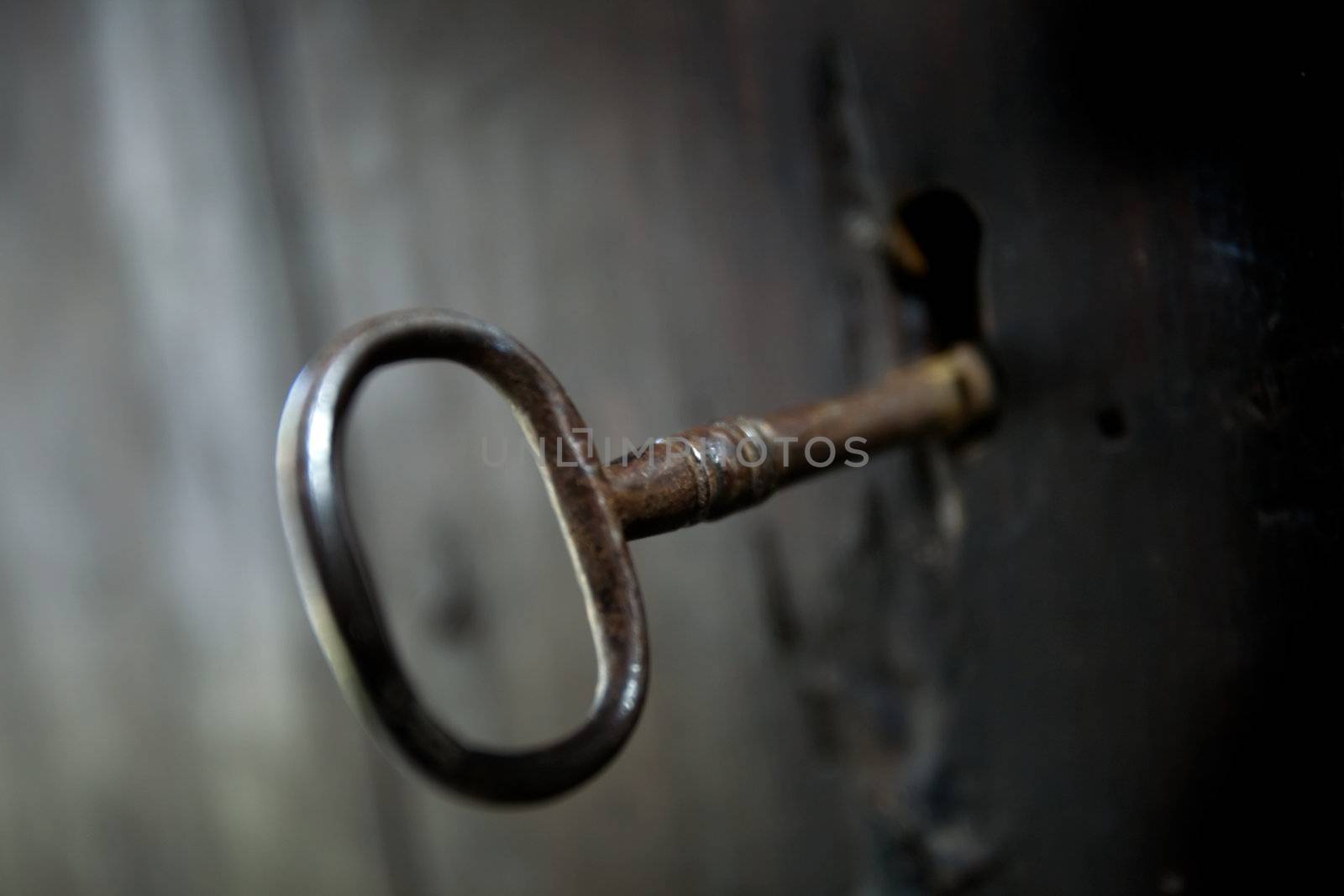 A skeleton key in a black door and lock.  Shallow depth of field.