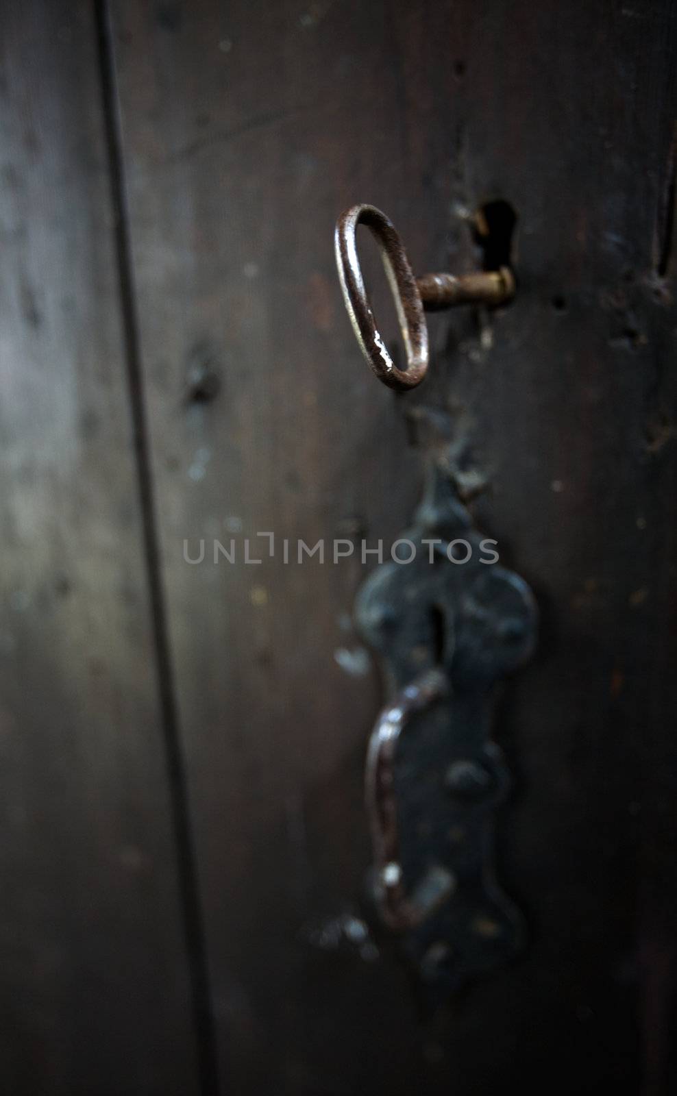 A skeleton key in a black door and lock.  Shallow depth of field.
