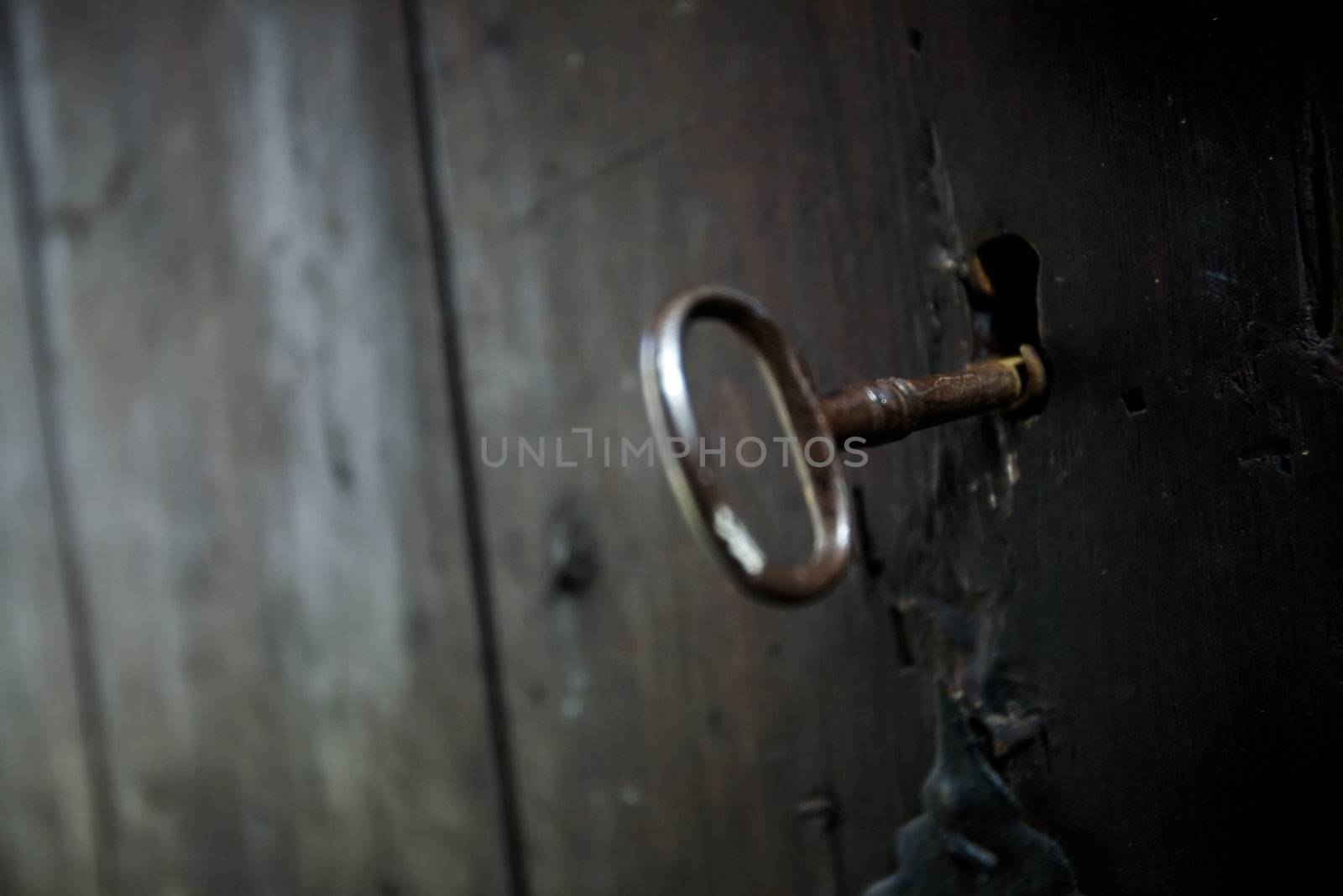 A skeleton key in a black door and lock.  Shallow depth of field with focus on key hole