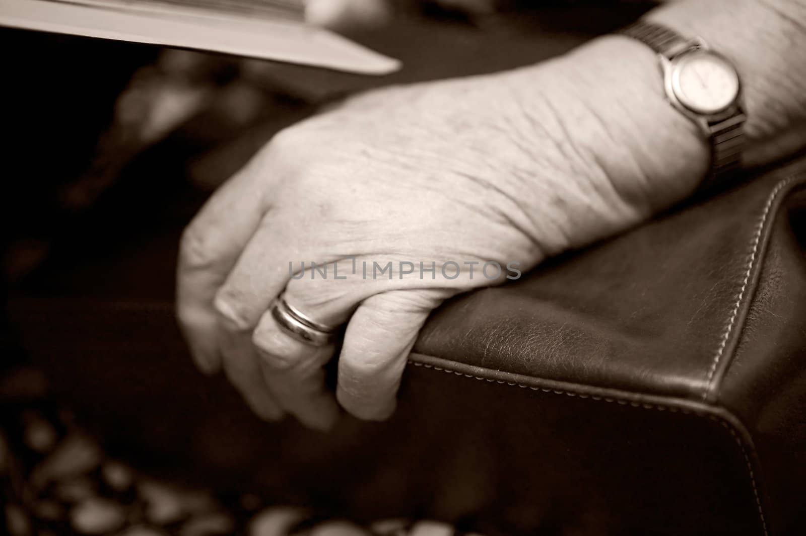 A detail of an old womans hand on her purse using shallow depth of field. The image is given a slight sepia toning