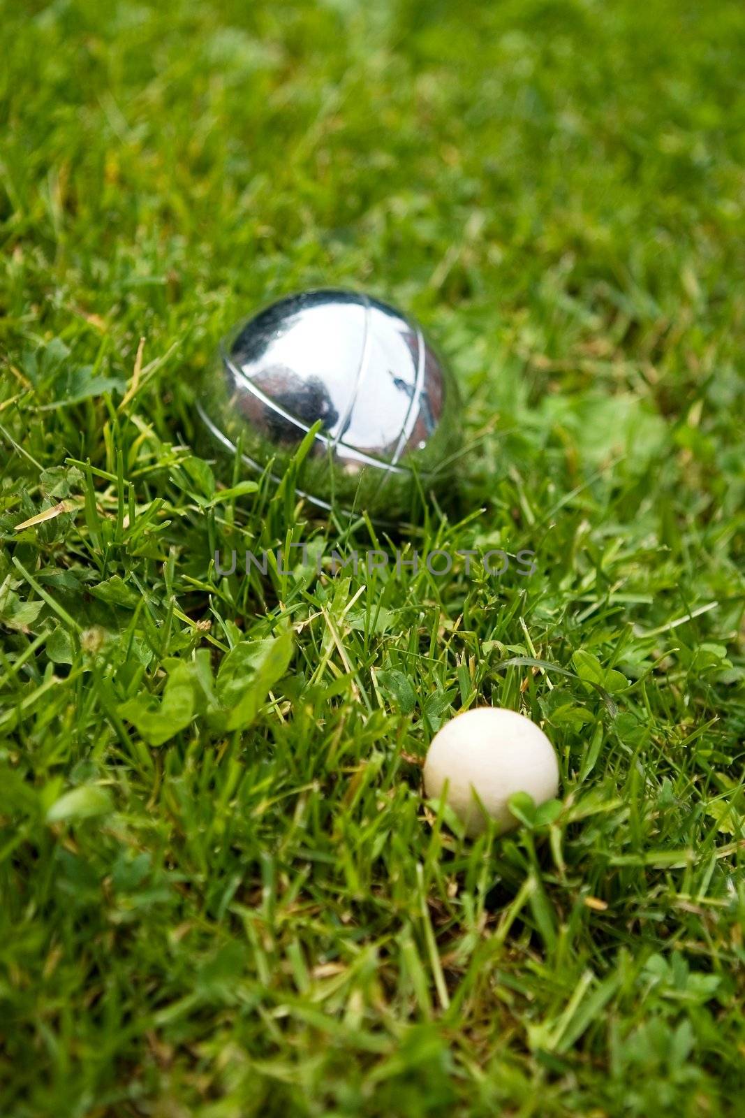 Bocce balls sitting in the green grass, close to the target. -shallow depth of field.-