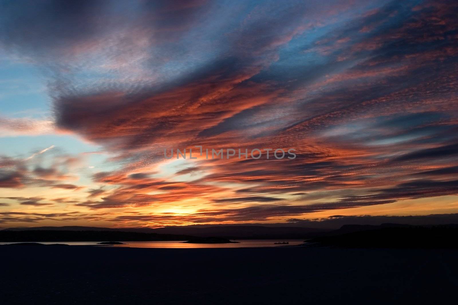 A golden sunset going down behind a hill over a frozen lake - fjord.  Oslo fjord in March.