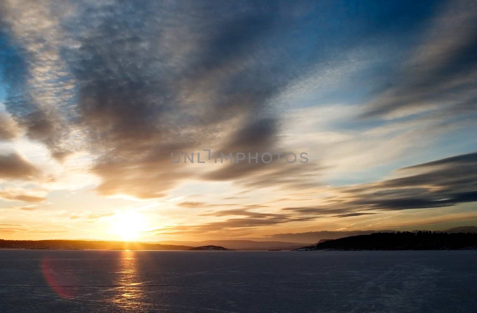 A golden sunset going down behind a hill over a frozen lake - fjord.  Oslo fjord in March.