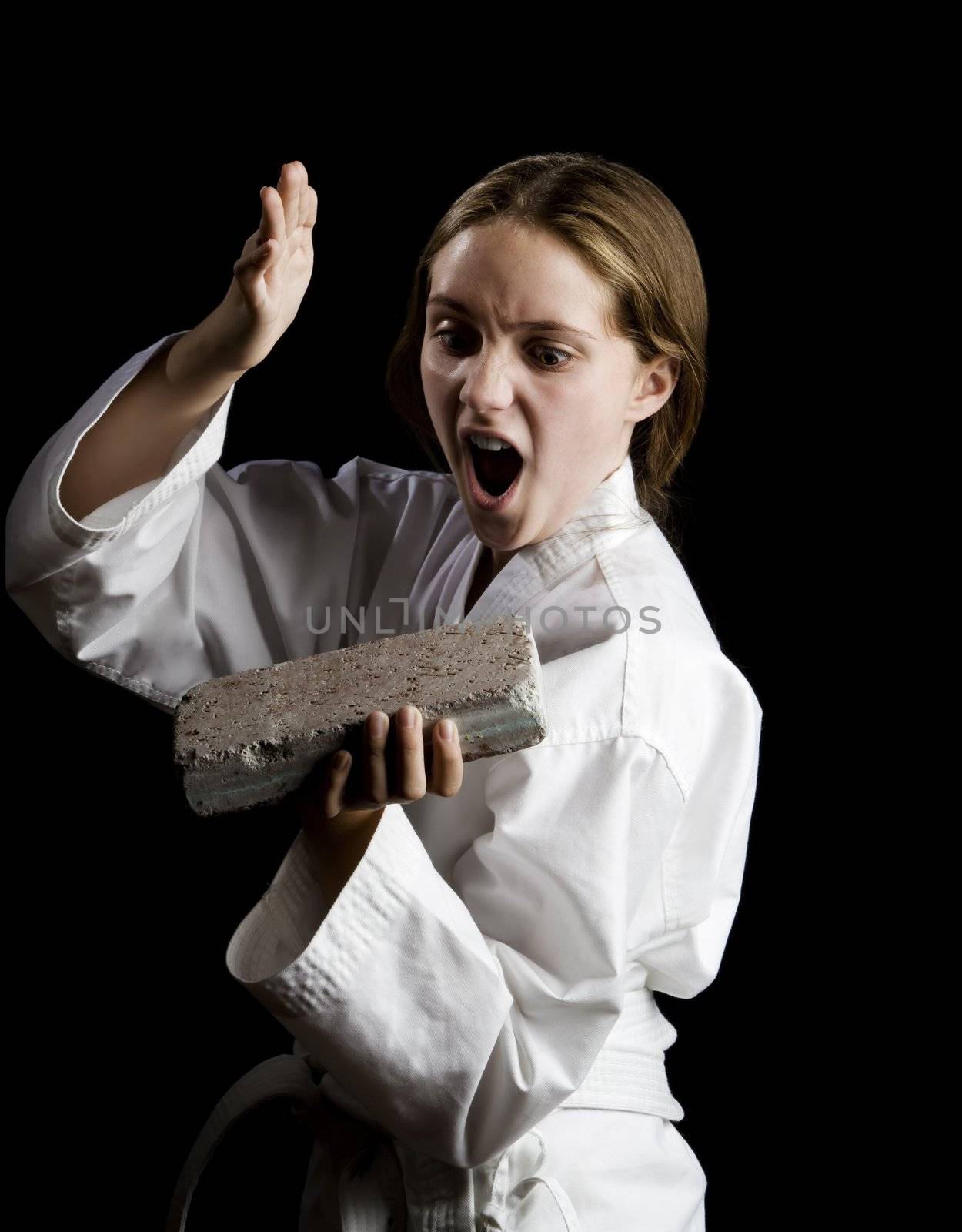 Young girl karate chopping a brick on black background