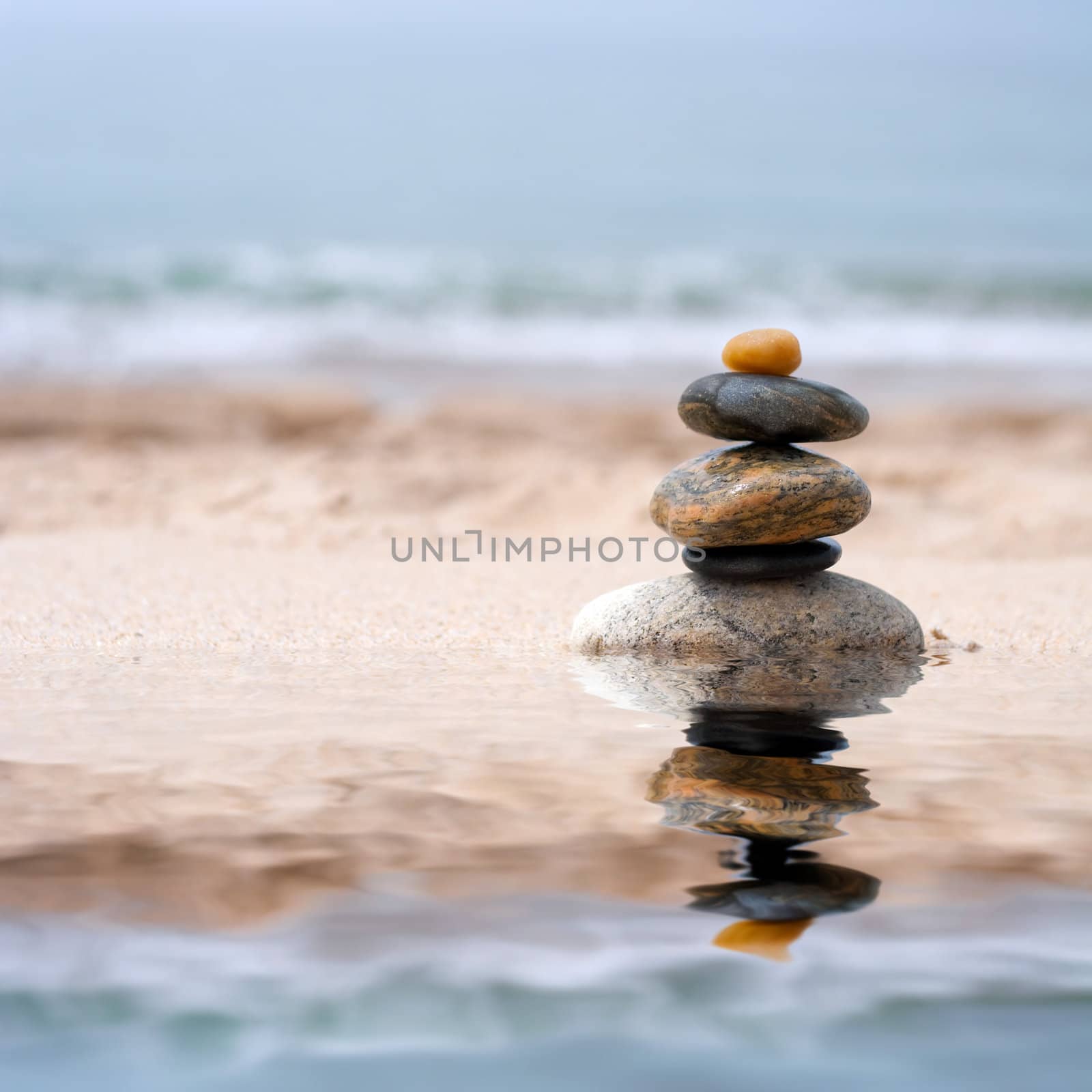 A pile of round smooth zen like stones stacked in the sand at the beach. 