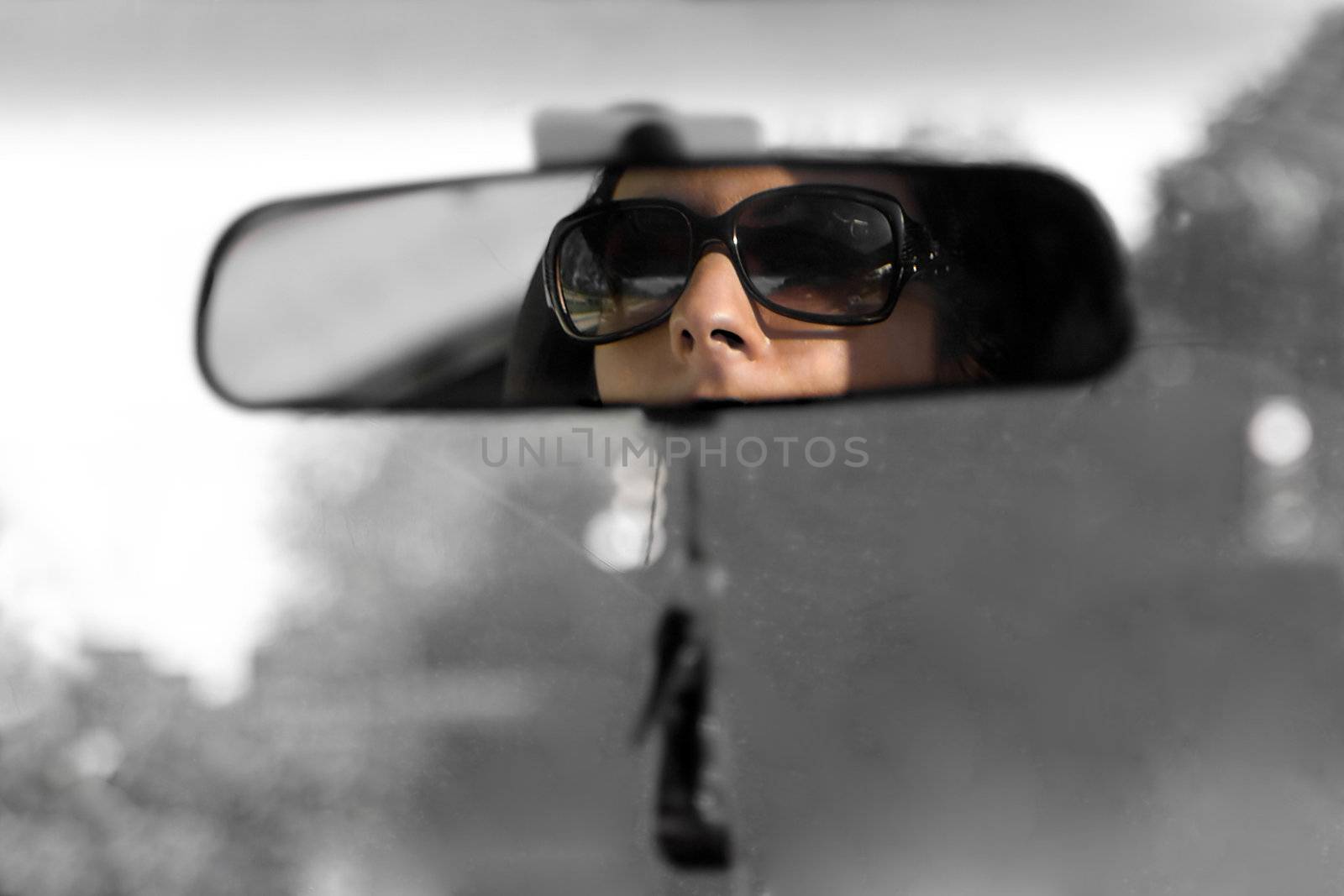 The face of a young woman driving as seen in the rear view mirror in isolated color.