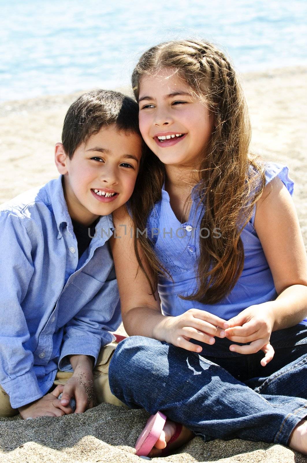 Portrait of brother and sister sitting on sand at the beach